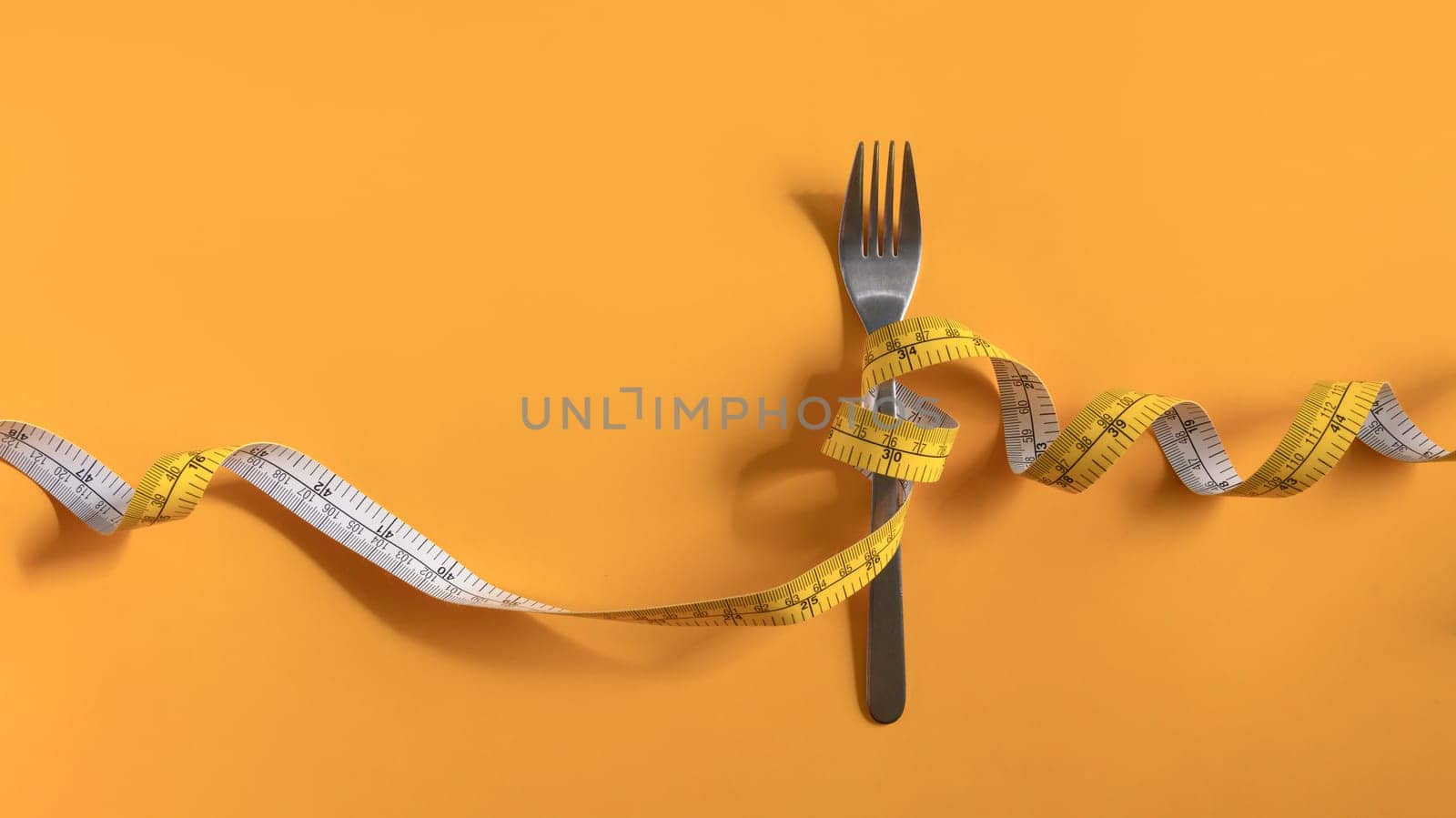 Fork with measuring tape on yellow background. Weight loss and healthy concept.