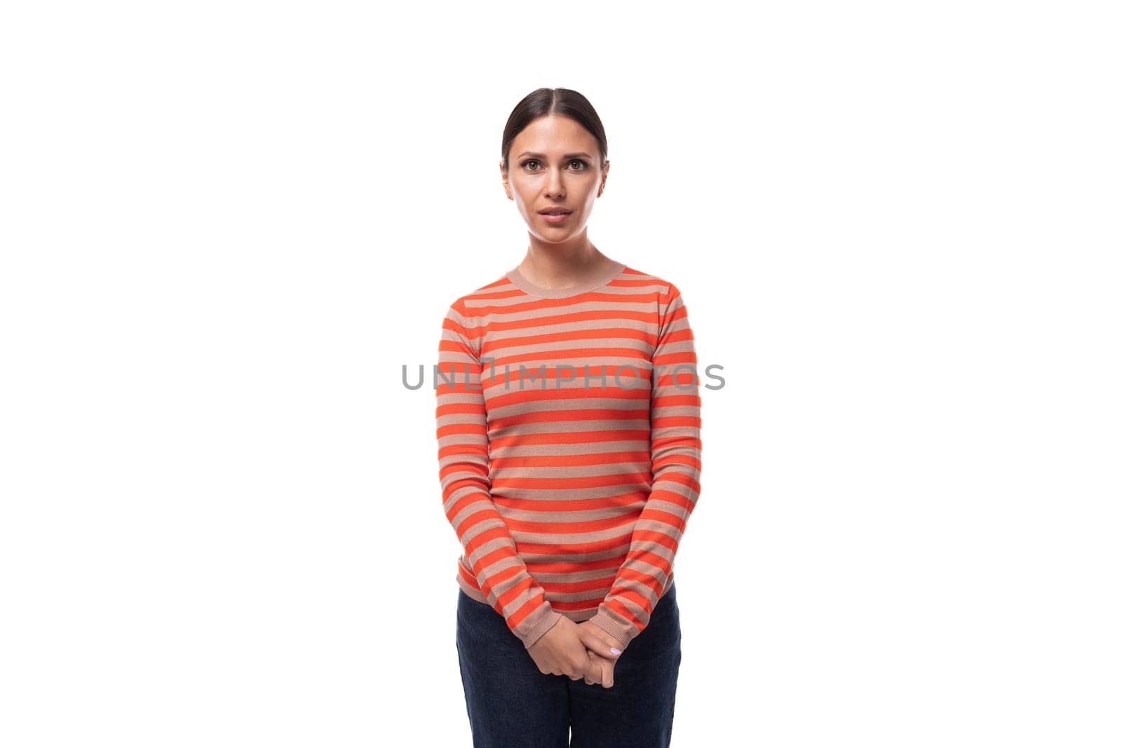 Young attentive slender brunette woman dressed in a striped orange jacket and jeans thought by TRMK