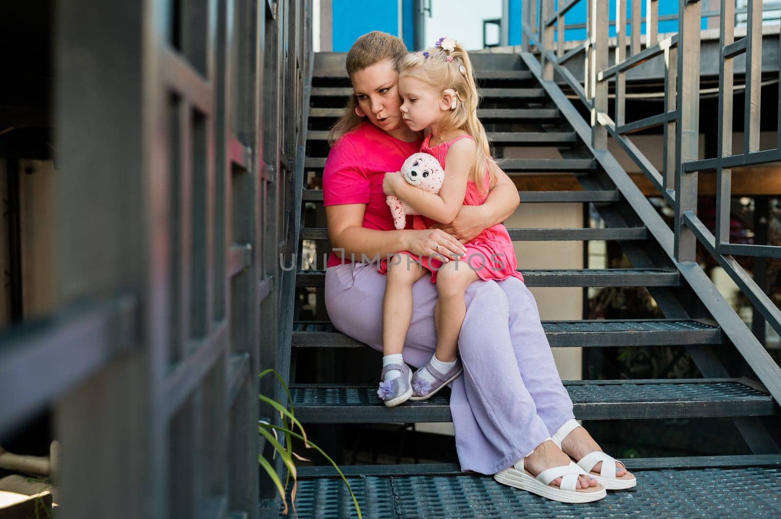 Mother holds and have fun her child with hearing aids and cochlear implants summer outdoor . Deaf and health concept. Diversity and inclusion. Copy space.