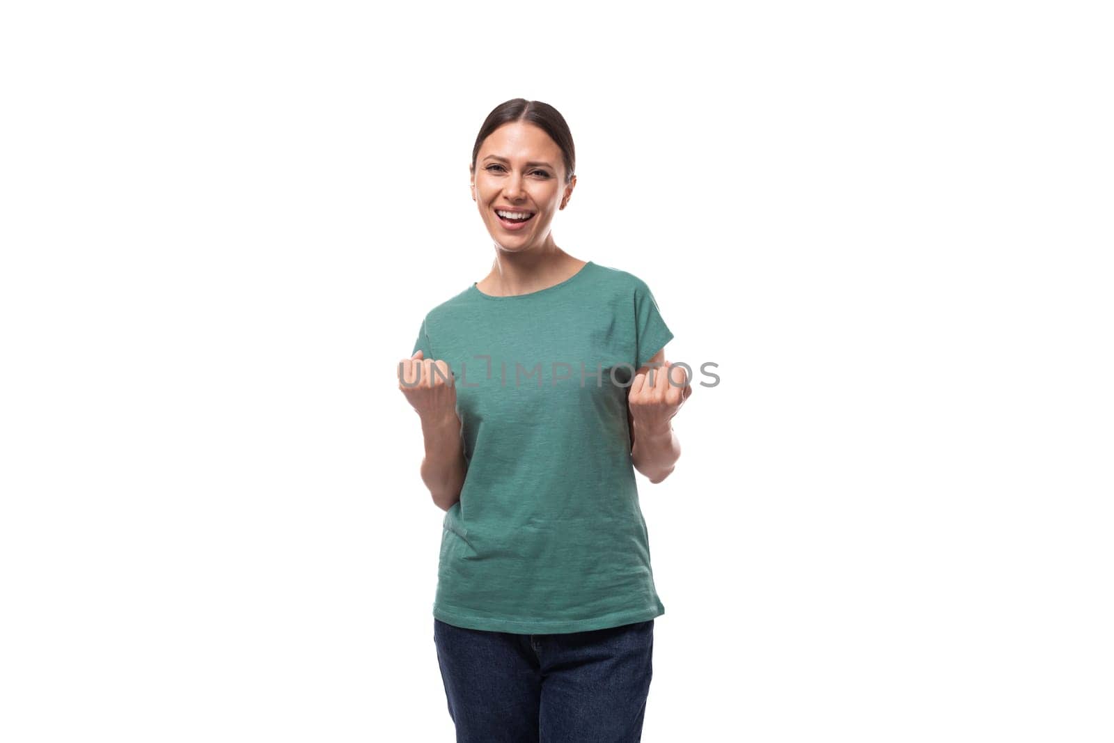 30 year old brunette woman with ponytail dressed in a green basic t-shirt smiling on a white background with copy space.