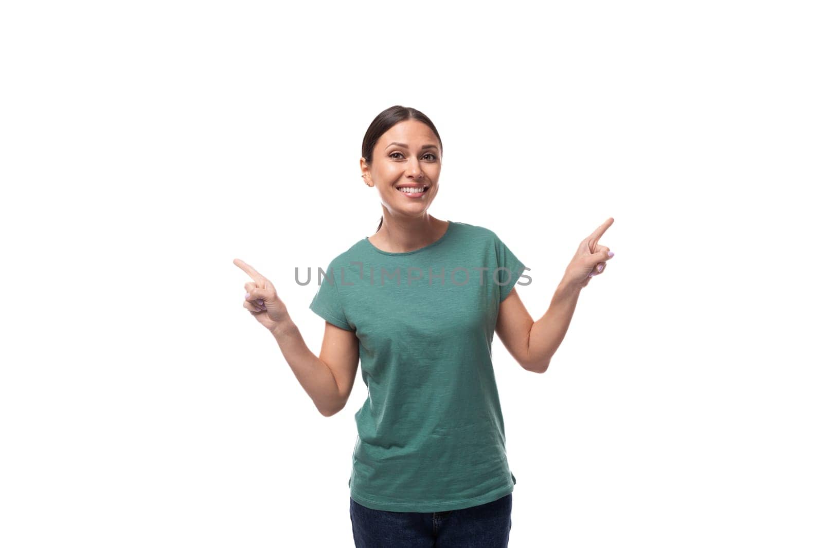 young beautiful brunette woman dressed in a green t-shirt points with her hand at copy space on a white background.