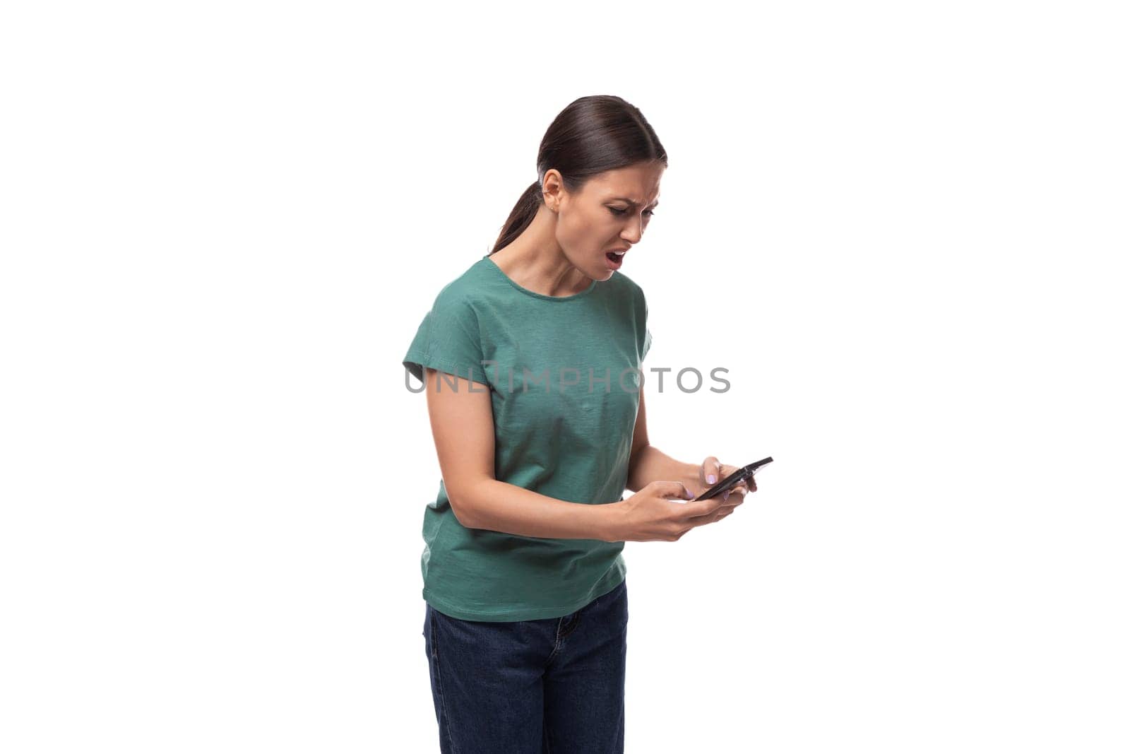 surprised young brunette woman dressed in green t-shirt and jeans uses smartphone by TRMK