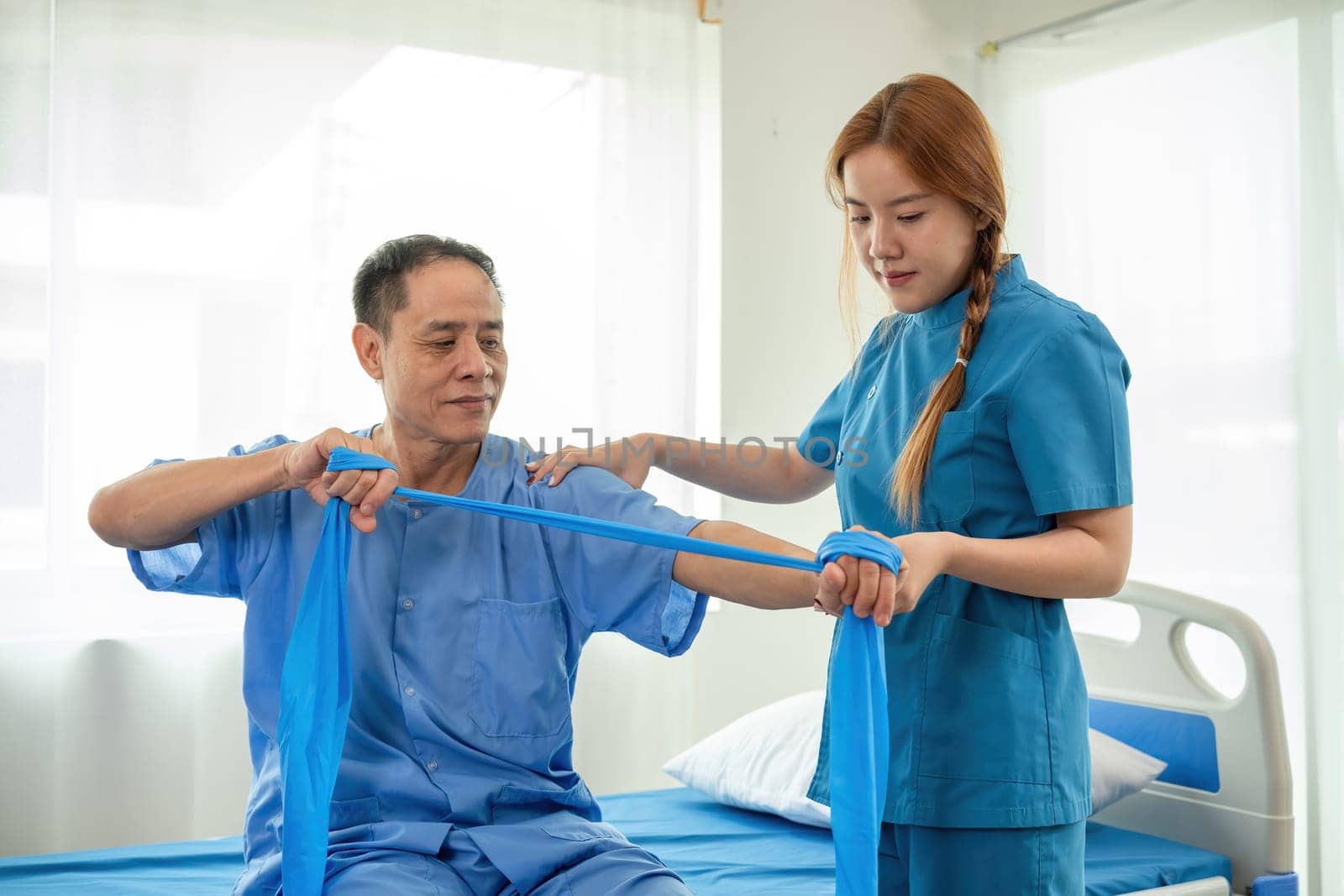 A sick caregiver or young nurse is helping a patient who is rehabilitating with physical therapy at the hospital. by wichayada