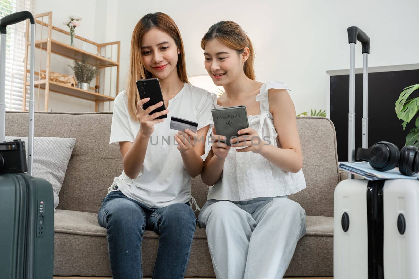 Two young female friends pack a suitcase with clothes and travel passports in preparation for a weekend away. by wichayada