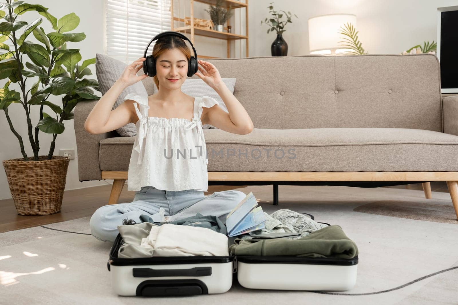 beautiful young woman happy Wear headphones to listen to music while packing your suitcase. by wichayada