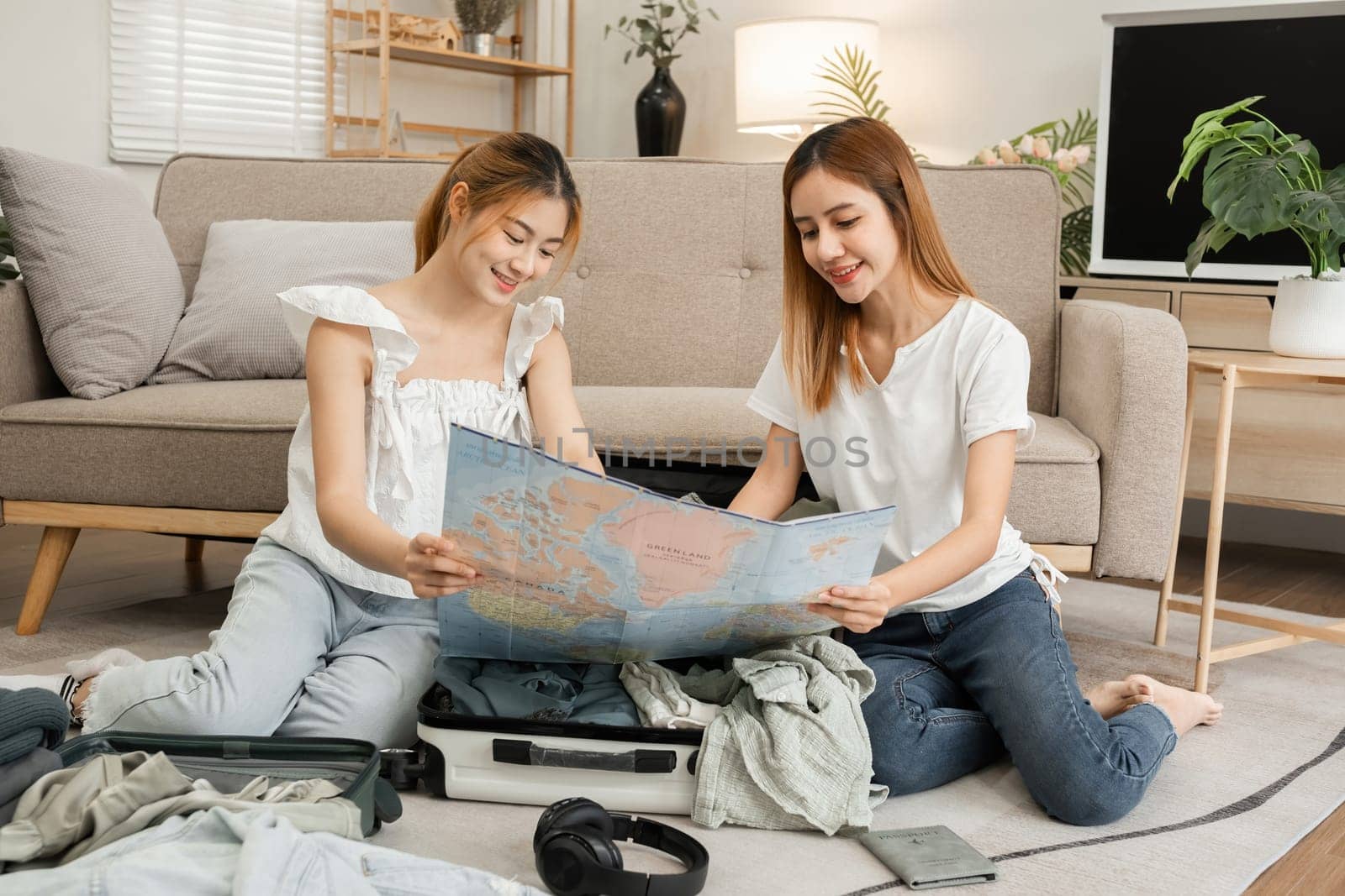 Two young female friends have fun packing supplies and clothes and discussing plans for a vacation together. by wichayada