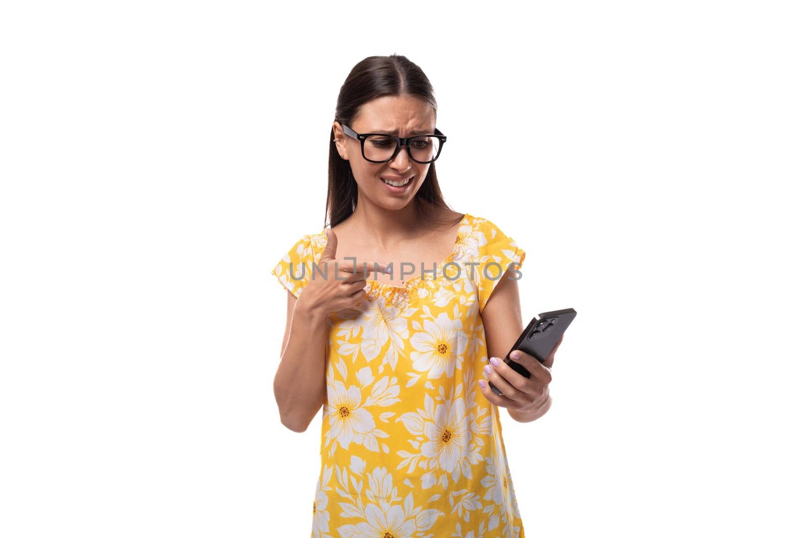 young smiling brunette woman with glasses dressed in a summer orange T-shirt looks carefully at the phone by TRMK