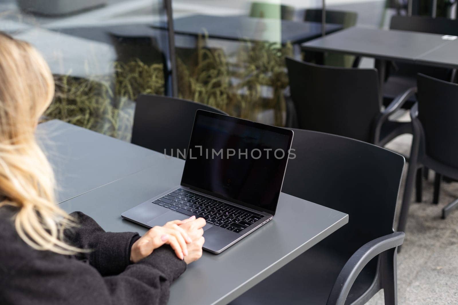 Young woman sitting on online meeting in outdoor cafe, talking to laptop camera, explaining something, drinking coffee. by Andelov13