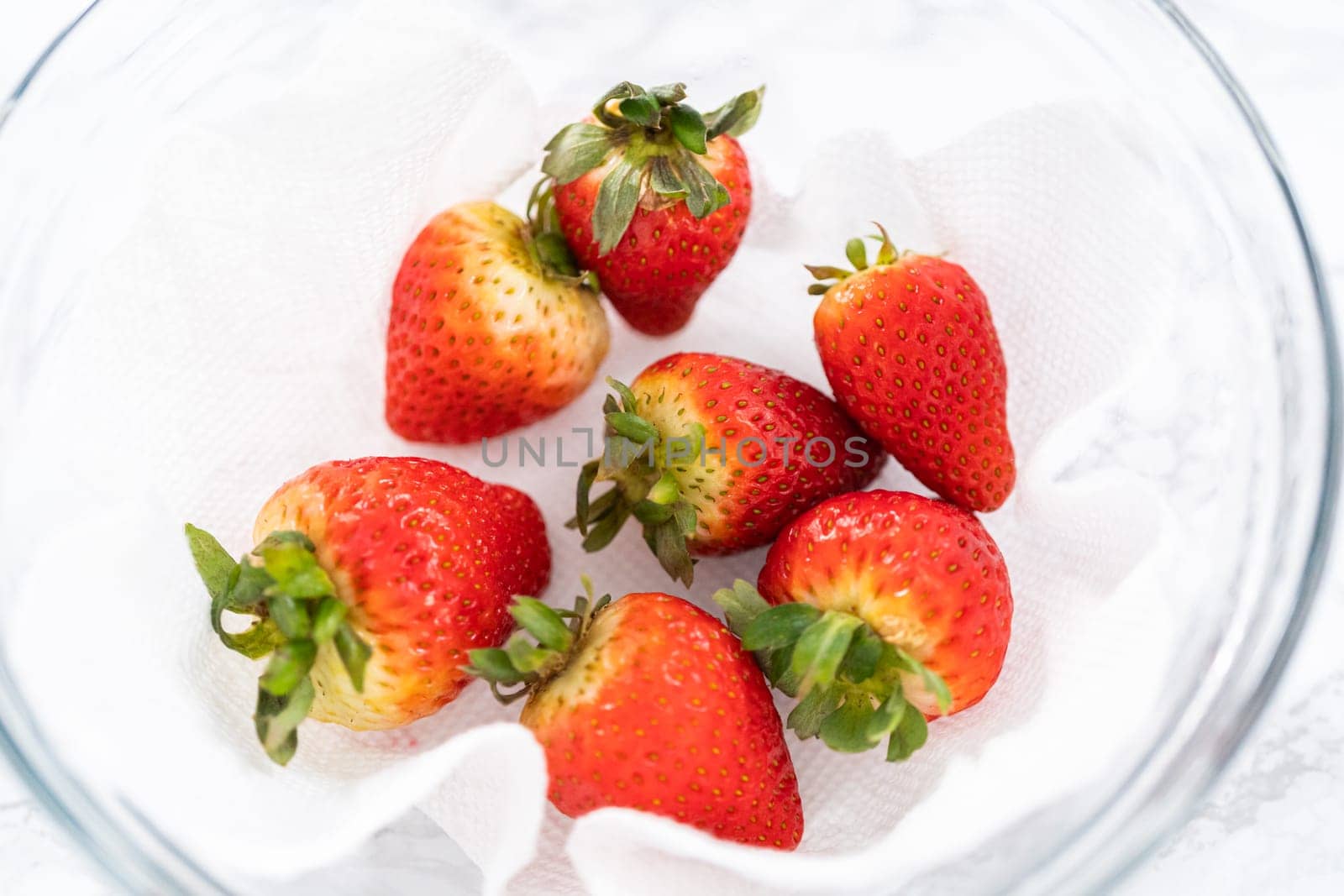 Freshly washed and dried strawberries are carefully arranged in a glass bowl lined with paper towel, ready for snacking or further use.