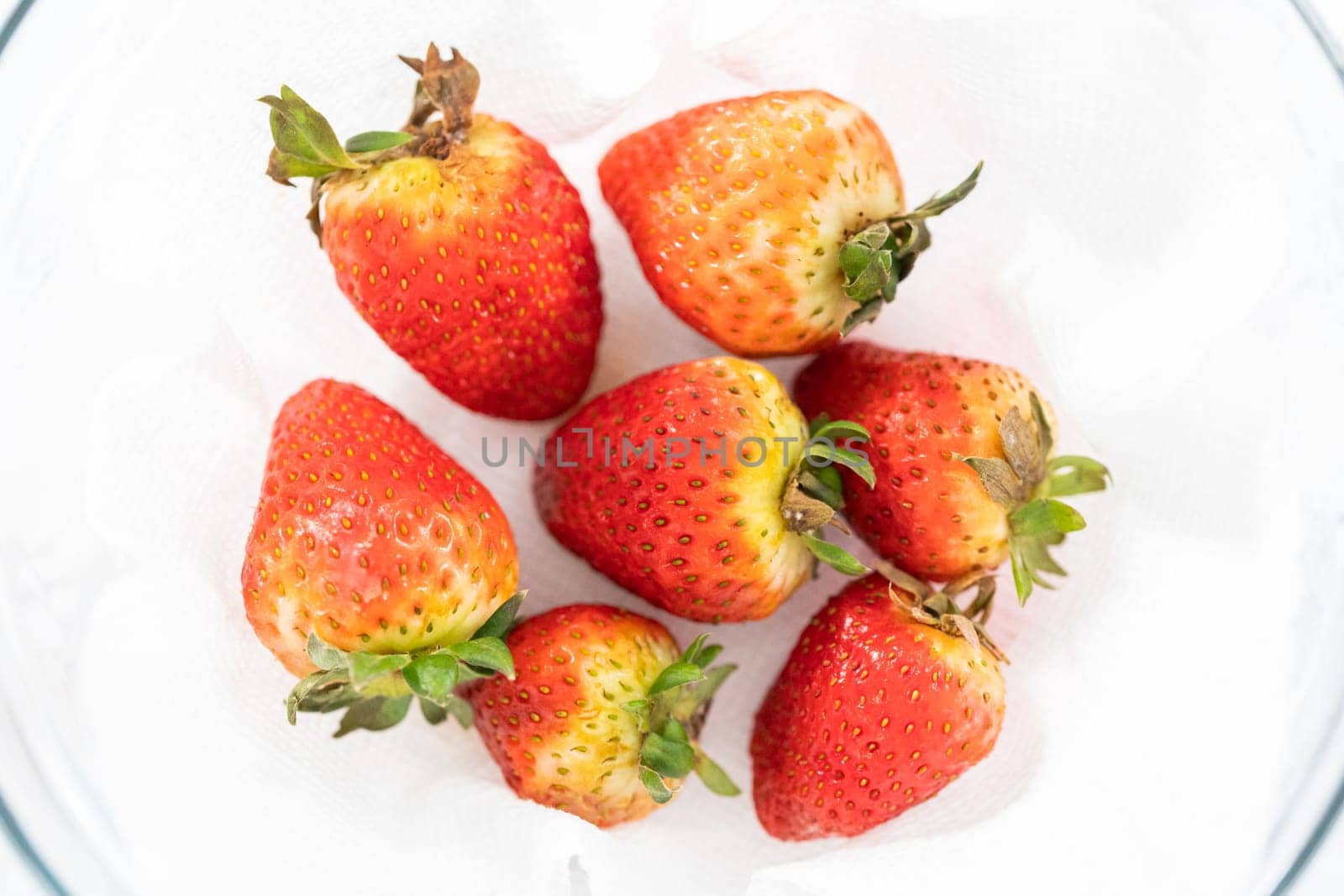 Freshly washed and dried strawberries are carefully arranged in a glass bowl lined with paper towel, ready for snacking or further use.