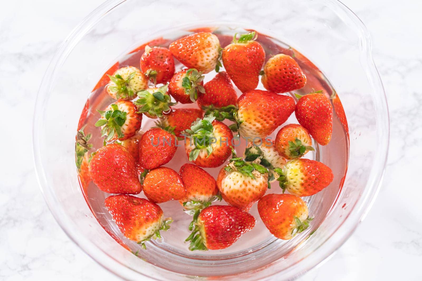 Preparing Strawberries in a Glass Mixing Bowl with Water by arinahabich