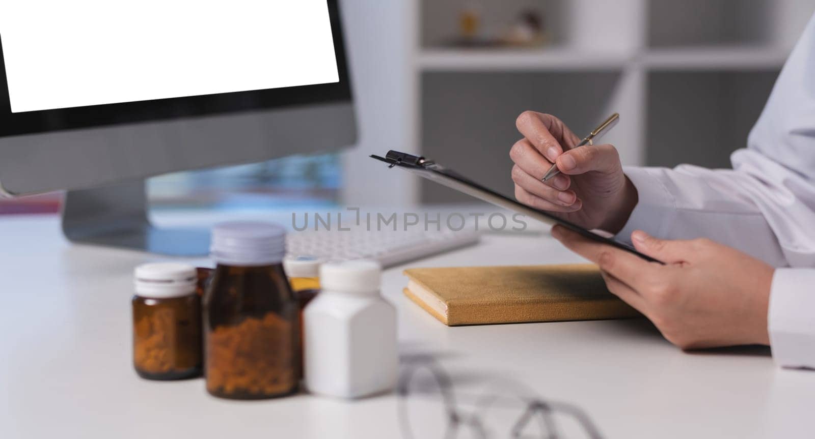 A doctor is writing on a clipboard in front of a computer monitor. The scene is set in a medical office with a desk and a computer. The doctor is using a pen to write on the clipboard