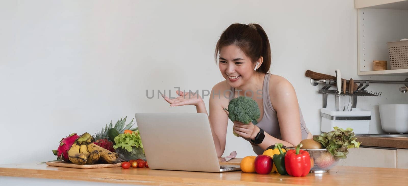 A woman is sitting at a table with a laptop and a bunch of vegetables. She is smiling and she is enjoying herself