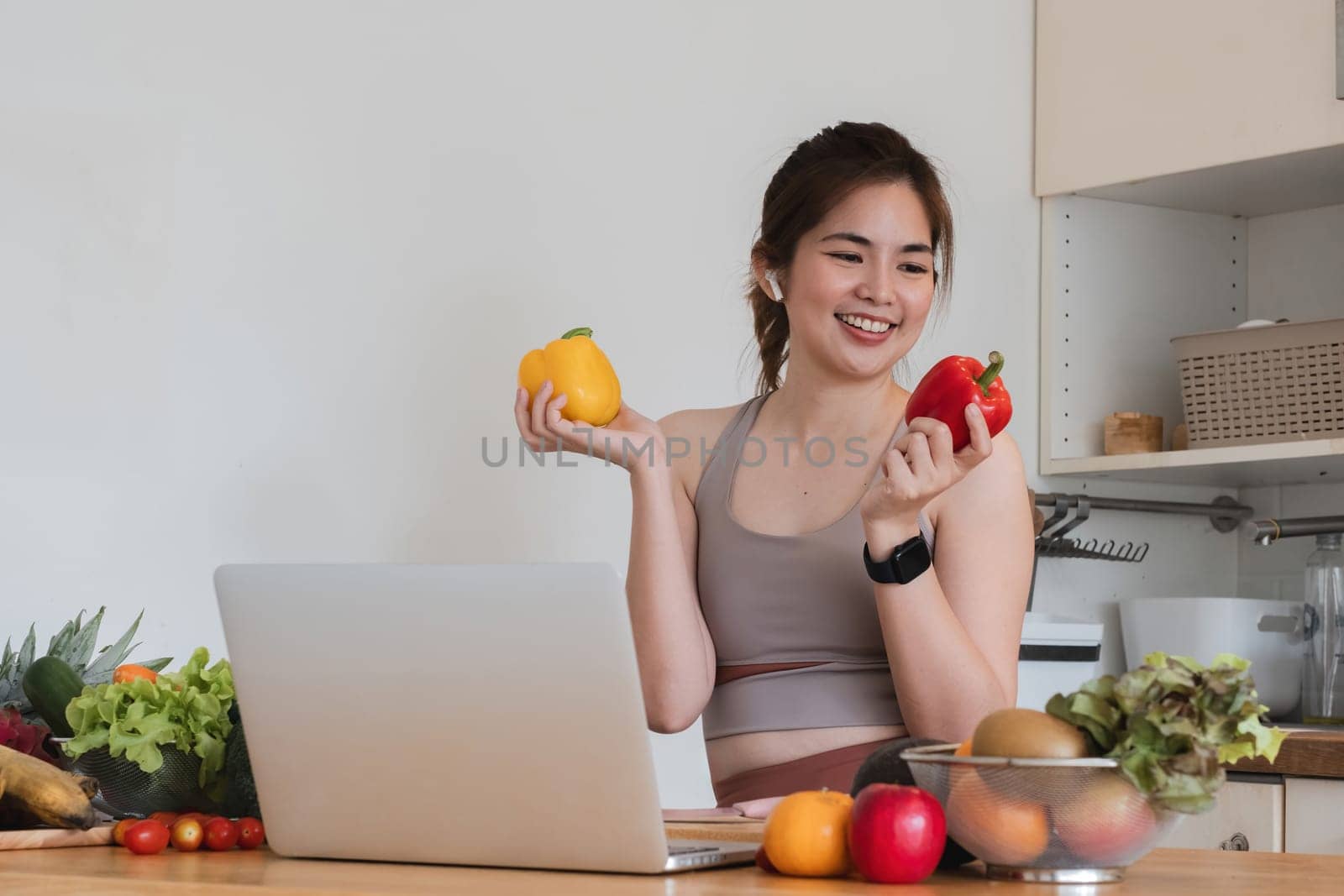 A woman is holding a laptop and two peppers in her hands. She is smiling and she is enjoying herself