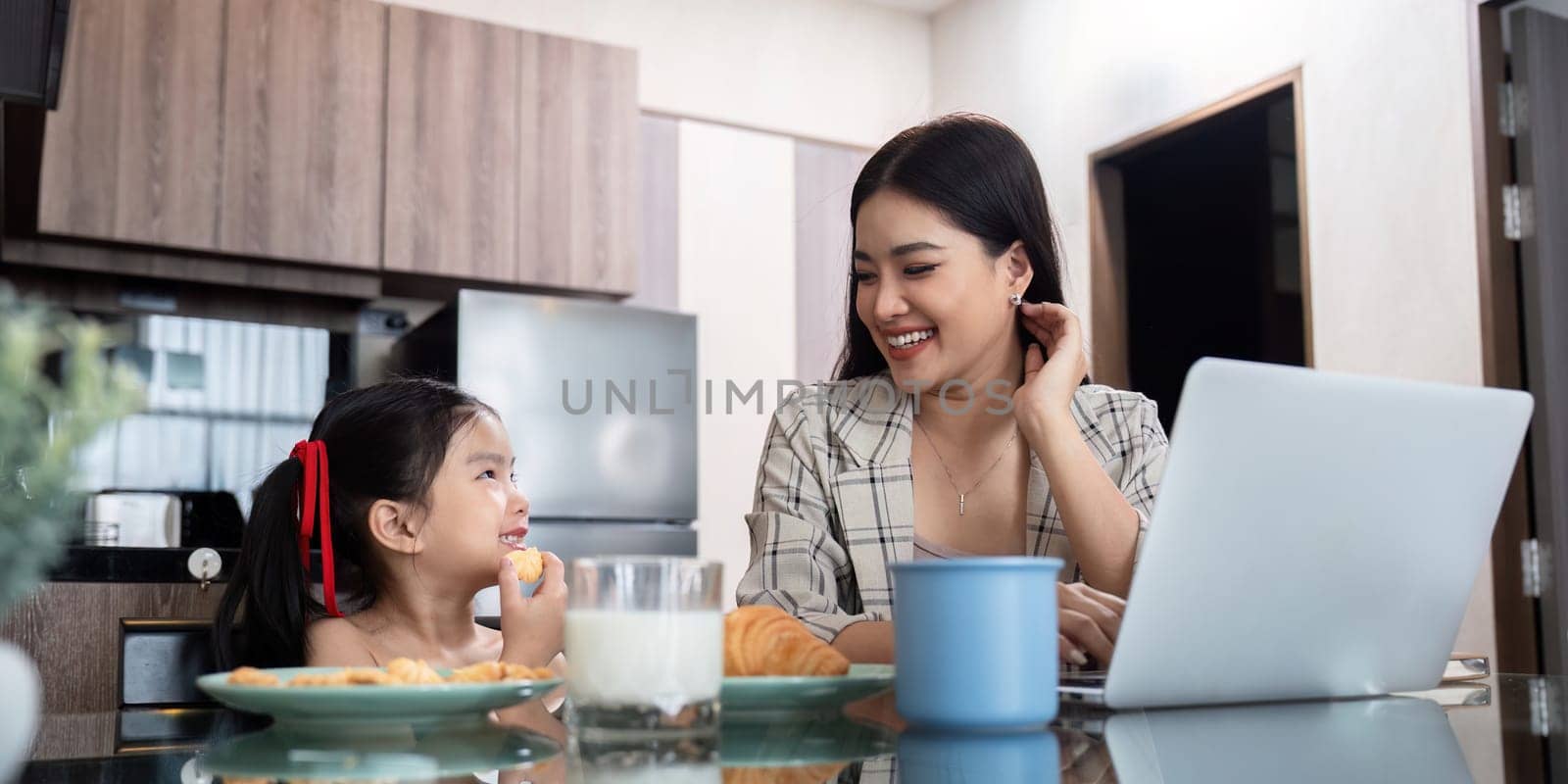 Working mom work from home office. Happy mother and daughter look to each other. businesswoman and cute child using laptop work freelancer workplace in living room by nateemee