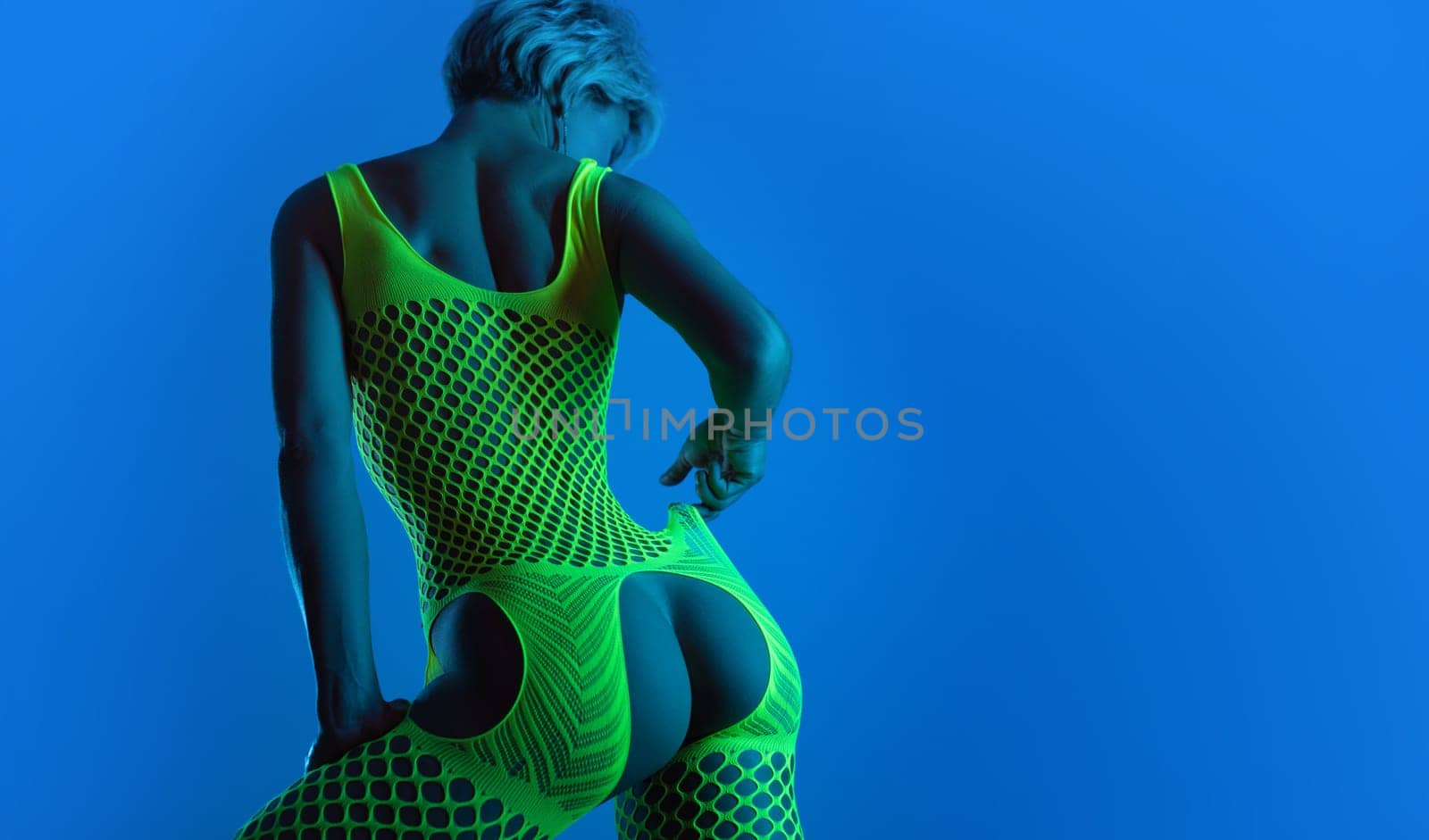 hot girl in erotic lingerie, a mesh bodysuit with an open crotch sexually poses with buttocks for a sex shop in neon blue light against a background of copy paste