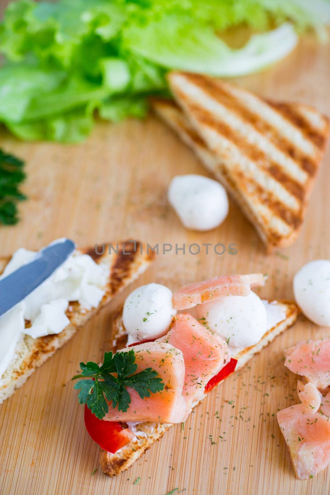 fried toast with salmon, cream cheese, salad, on a wooden table by Rawlik