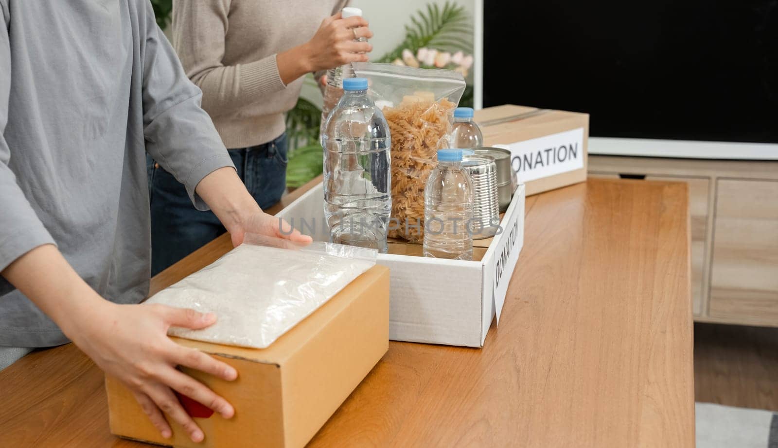 Two young female volunteers help pack food into donation boxes and prepare to donate them to charity.