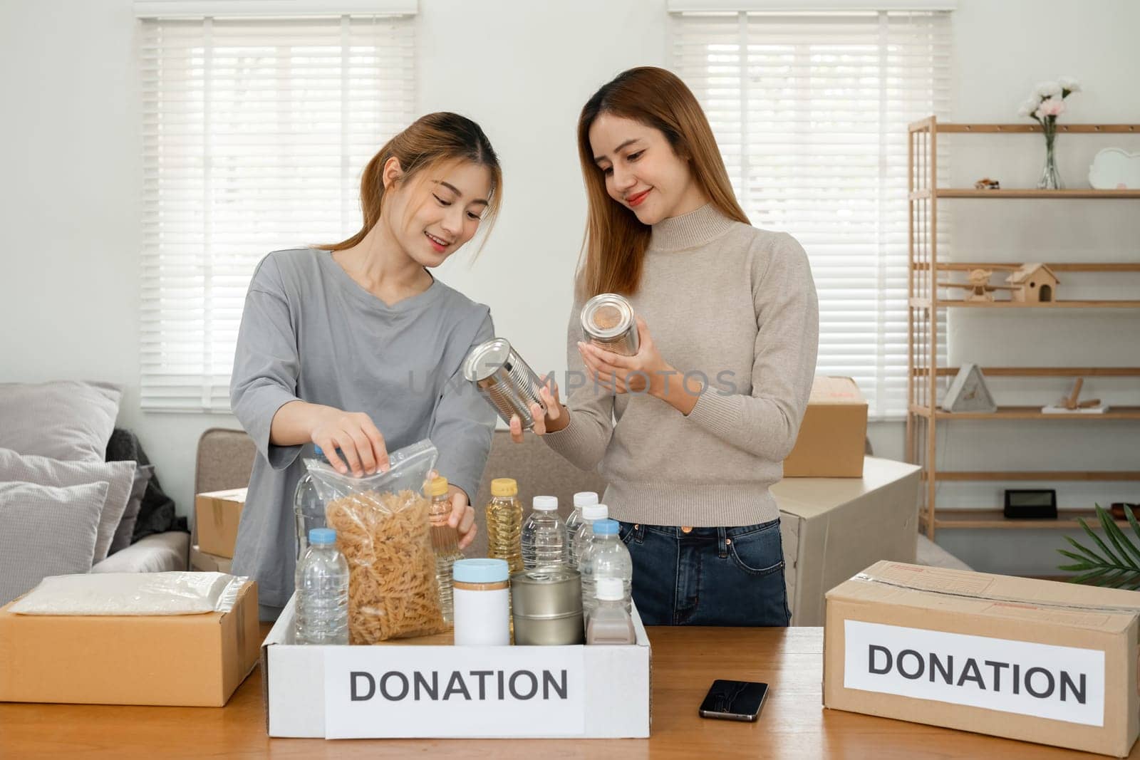 Two young female volunteers help pack food into donation boxes and prepare to donate them to charity.