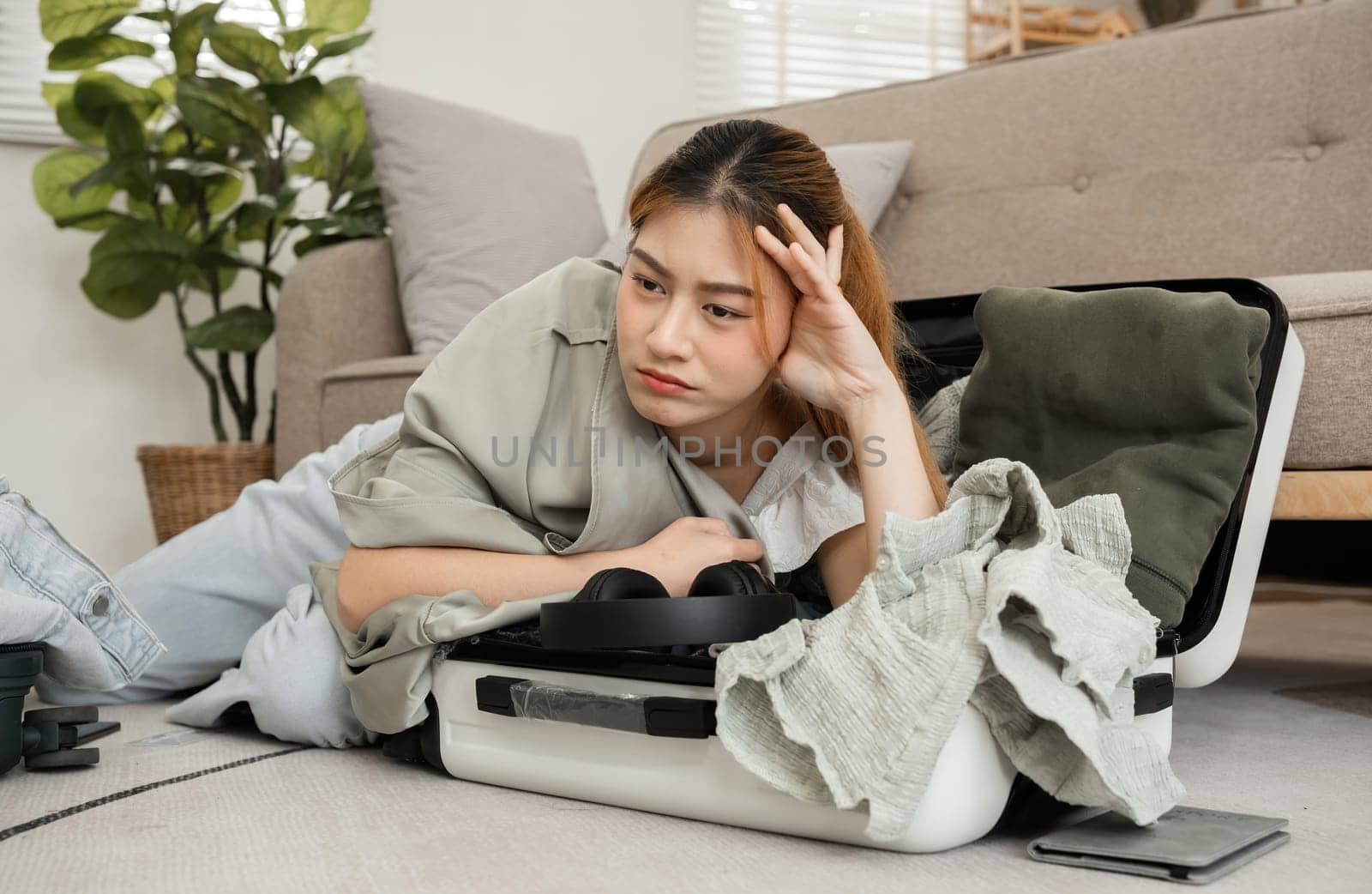 Asian female tourist is tired from packing her suitcase, checking her belongings and passport in preparation for her weekend trip..