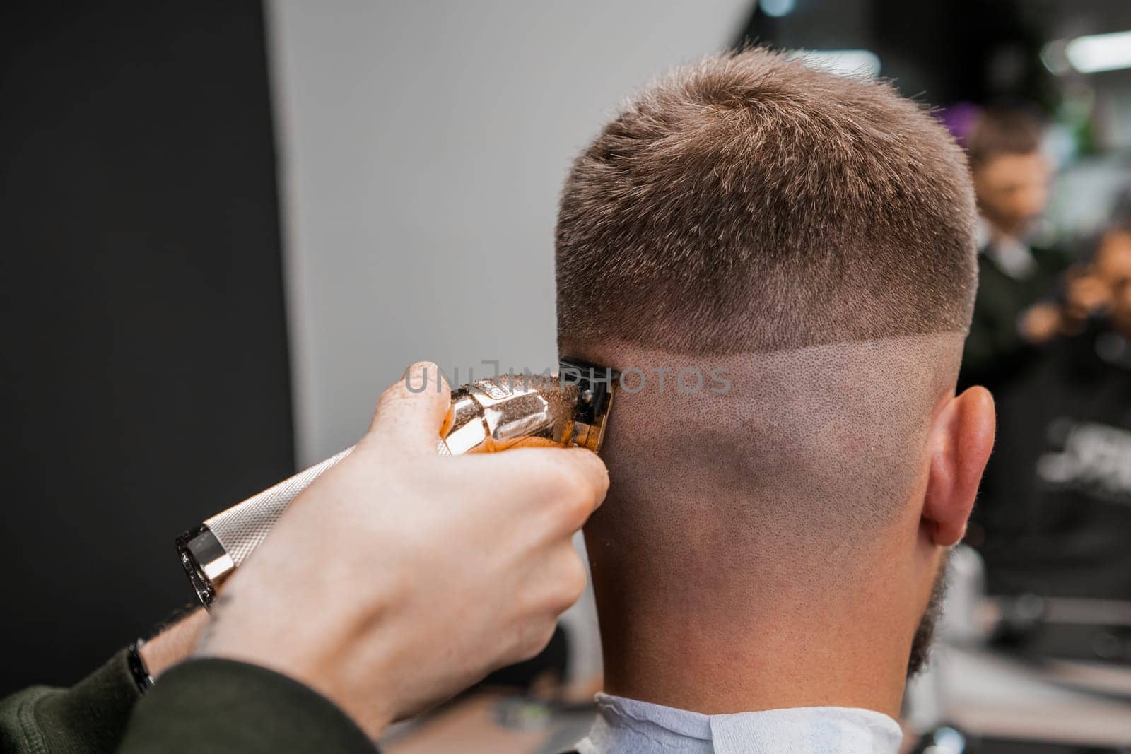 Barber trims the back of a mans head with a trimmer at the barbershop