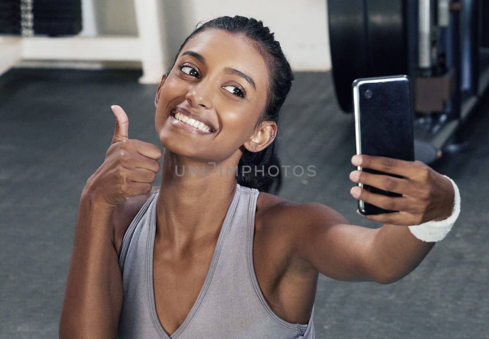 Woman, thumbs up and selfie on phone in gym for social media post or wellness blog in training. Happy, active and female person with mobile for sign of success workout or fitness session for health by YuriArcurs