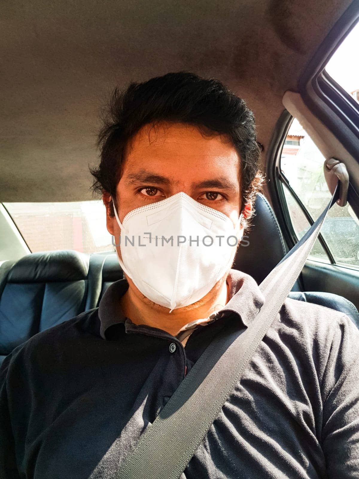 A man driving a car puts on a medical mask during an epidemic, a taxi driver in a mask, protection from the virus. by Peruphotoart