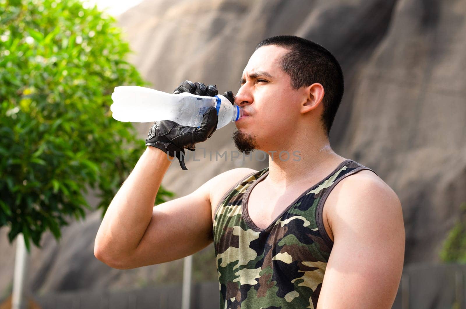 Young exhausted athlete drinking fresh water to cool off during a running track. by Peruphotoart