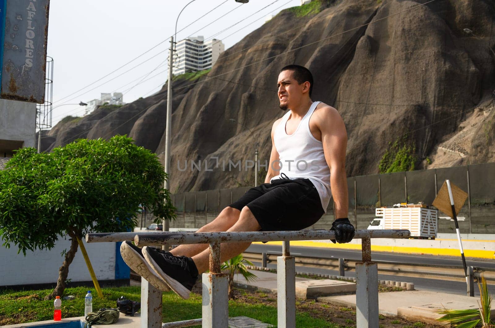 Handsome man exercising on parallel bars on the street outdoors. by Peruphotoart