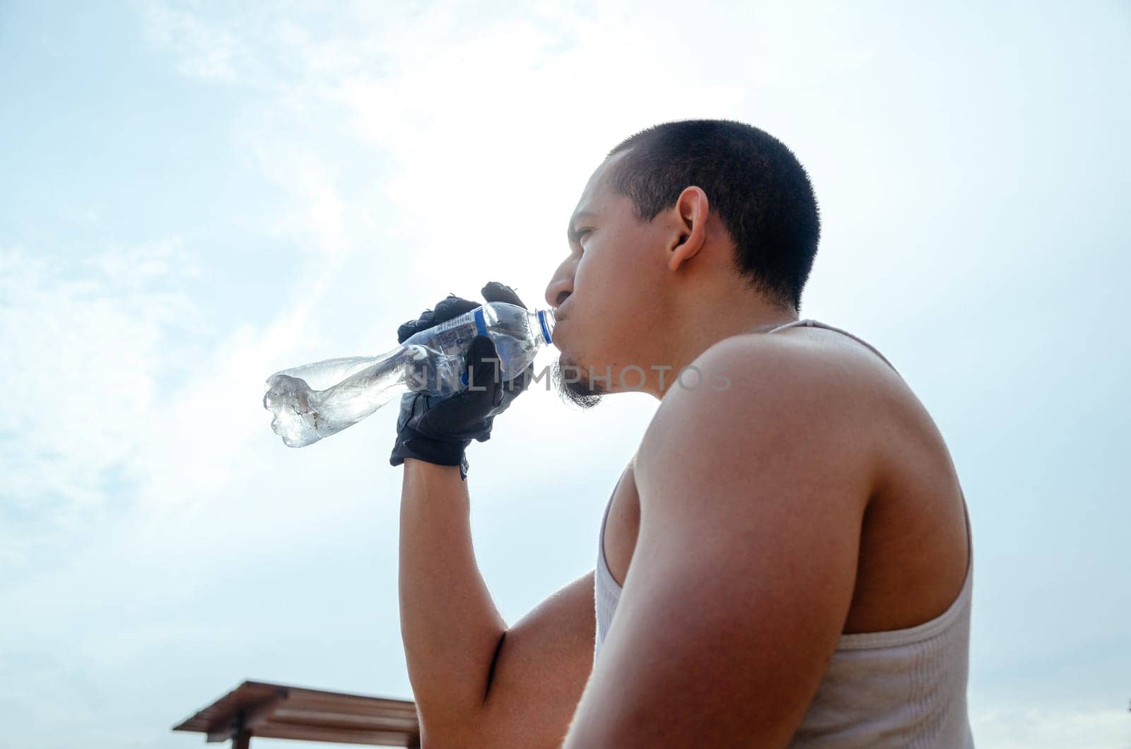 Young exhausted athlete drinking fresh water to cool off during a running track