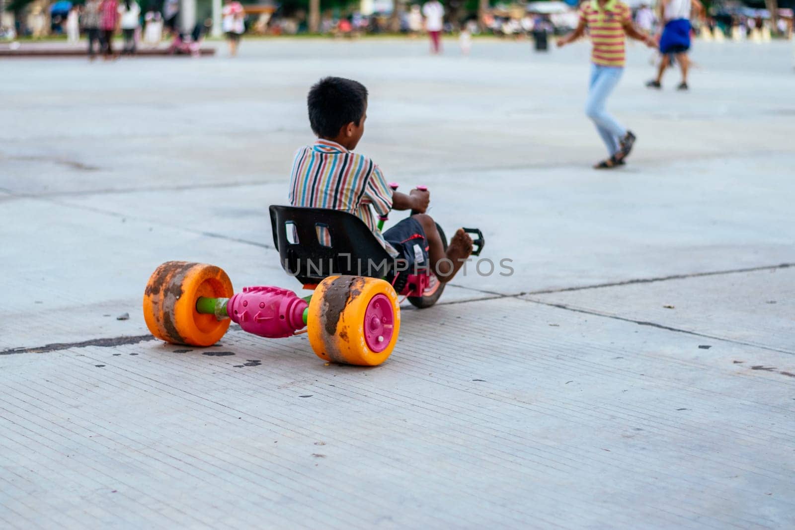 Unrecognizable boy with his back turned in the park driving a toy car before the pandemic. by Peruphotoart