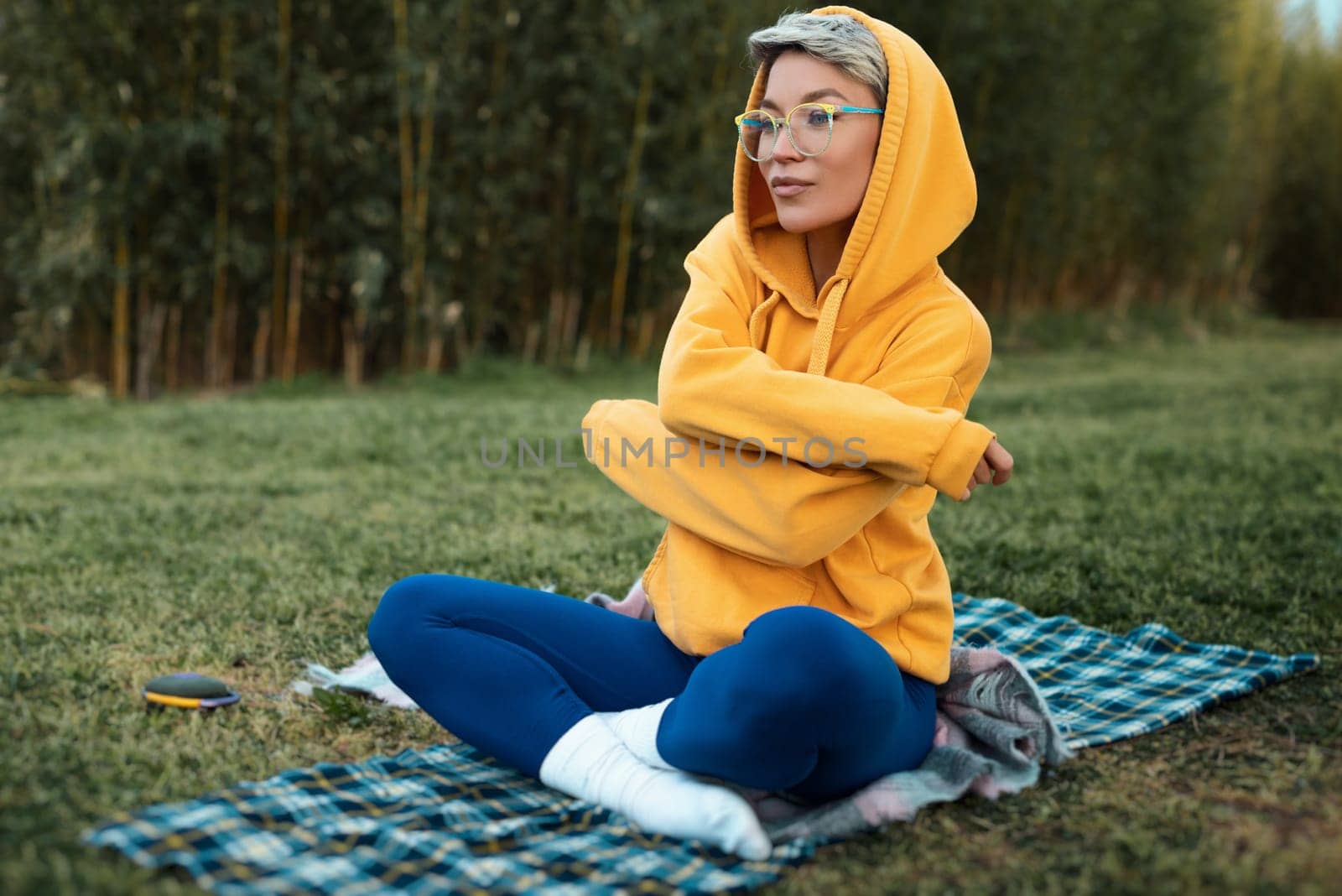 cute girl with glasses in an orange hoodie is sitting in a park in nature expressing kind emotions by Rotozey