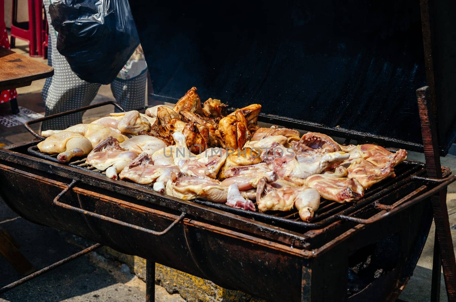 Chicken wing being grilled on a charcoal stove with smoke. Street food