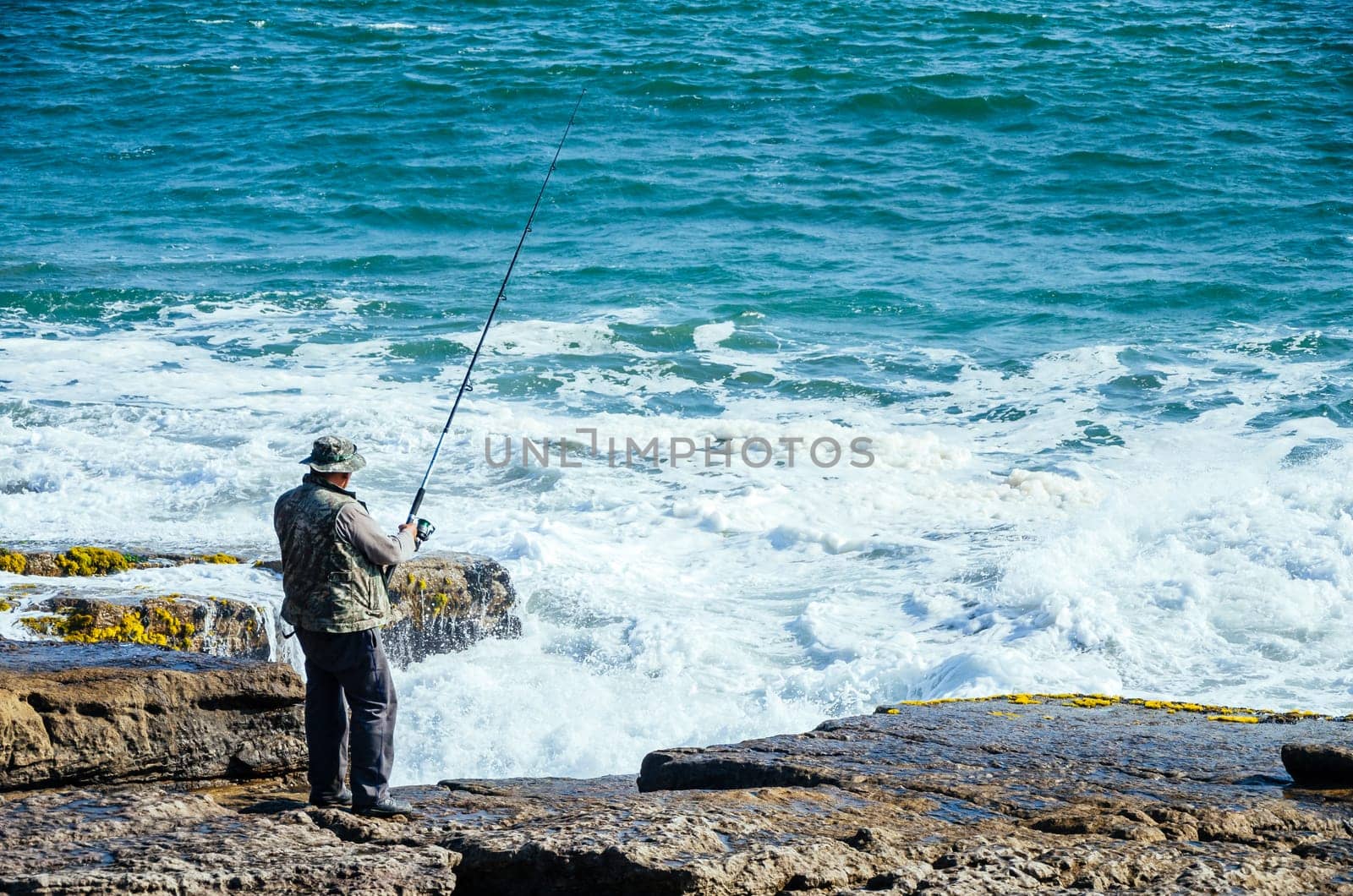 Fisherman with a fishing rod in the sea, fishing. by Peruphotoart