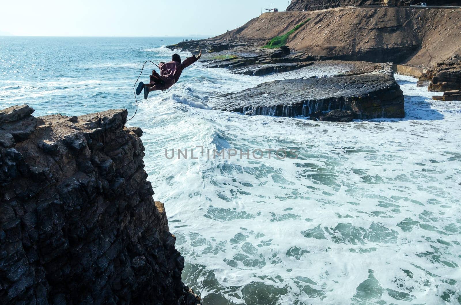 Man dressed as a friar throws himself off a cliff and head into the ocean at sunset. by Peruphotoart