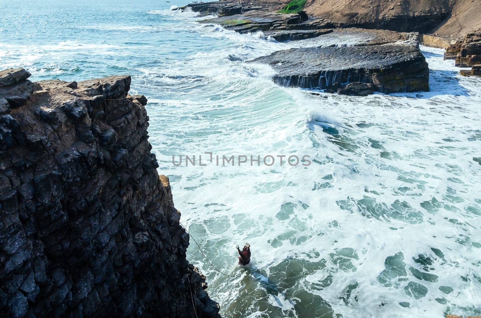 Man dressed as a friar throws himself off a cliff and head into the ocean at sunset
