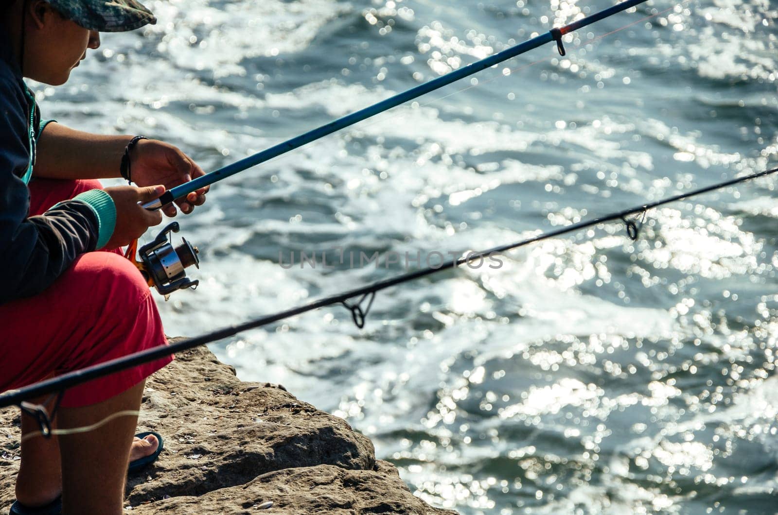 Fisherman sitting with a fishing rod in the sea, fishing. by Peruphotoart