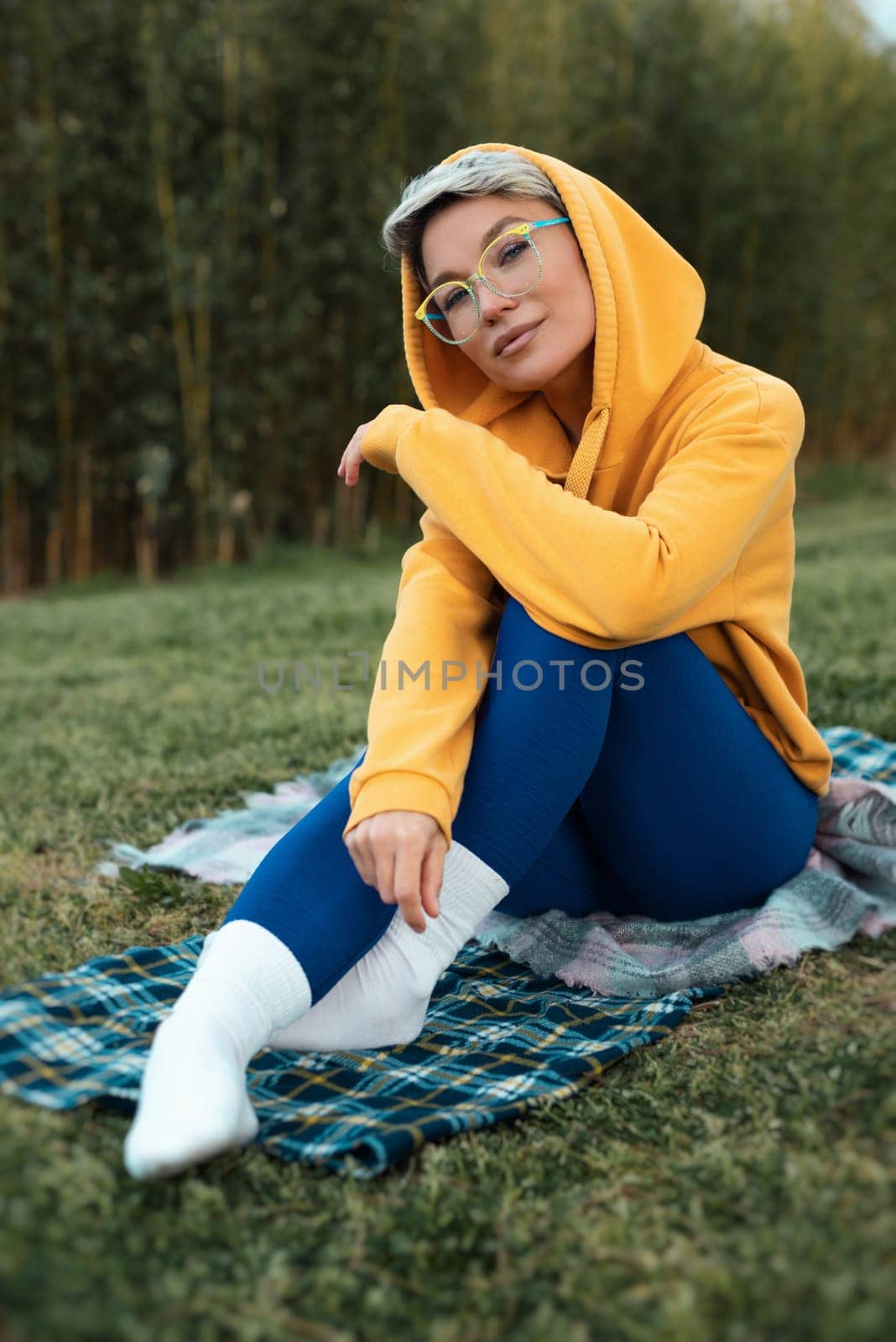 A cute girl with glasses in an orange hoodie is sitting in a park in nature expressing kind emotions