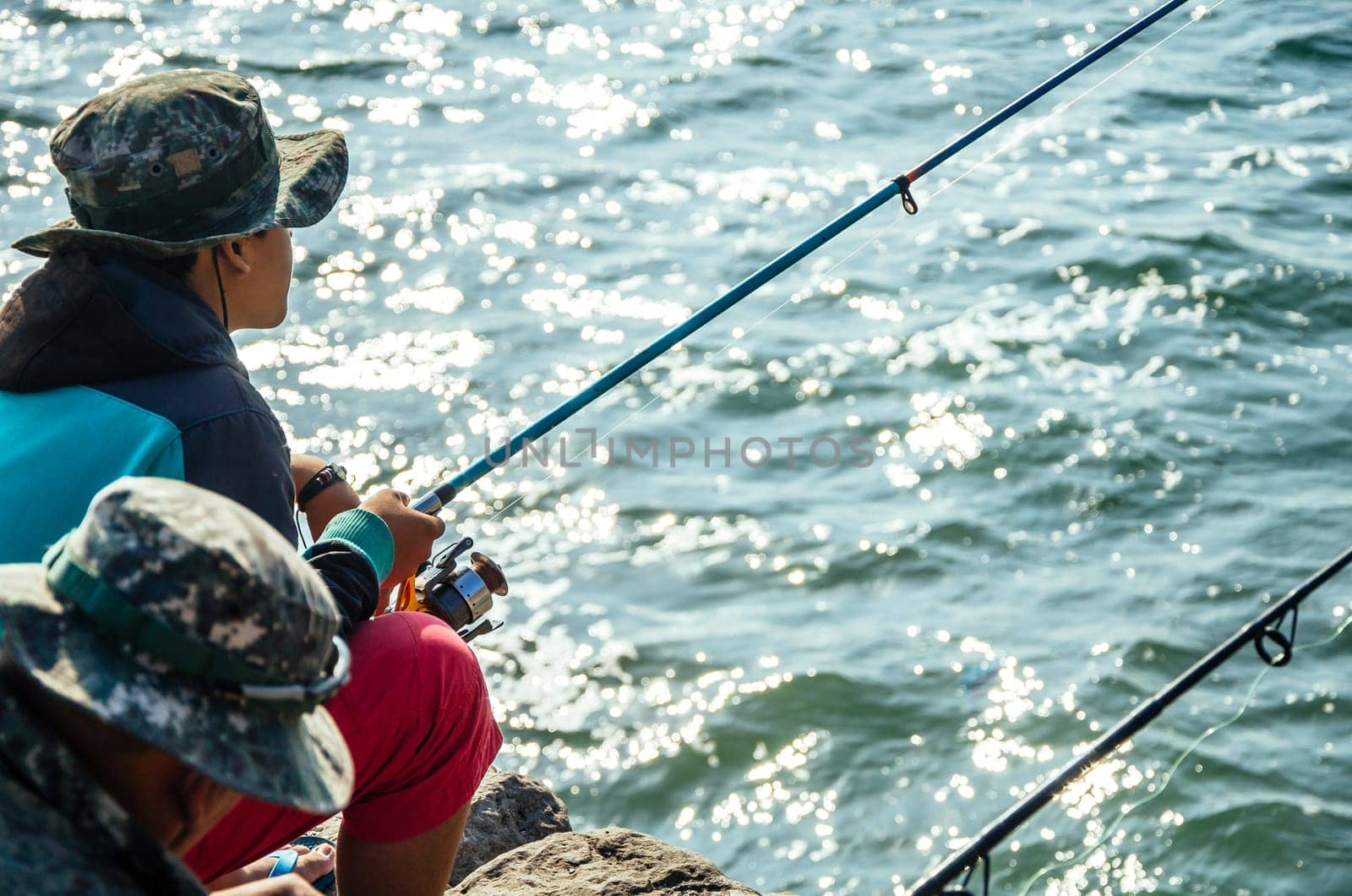 Fisherman sitting with a fishing rod in the sea, fishing. by Peruphotoart