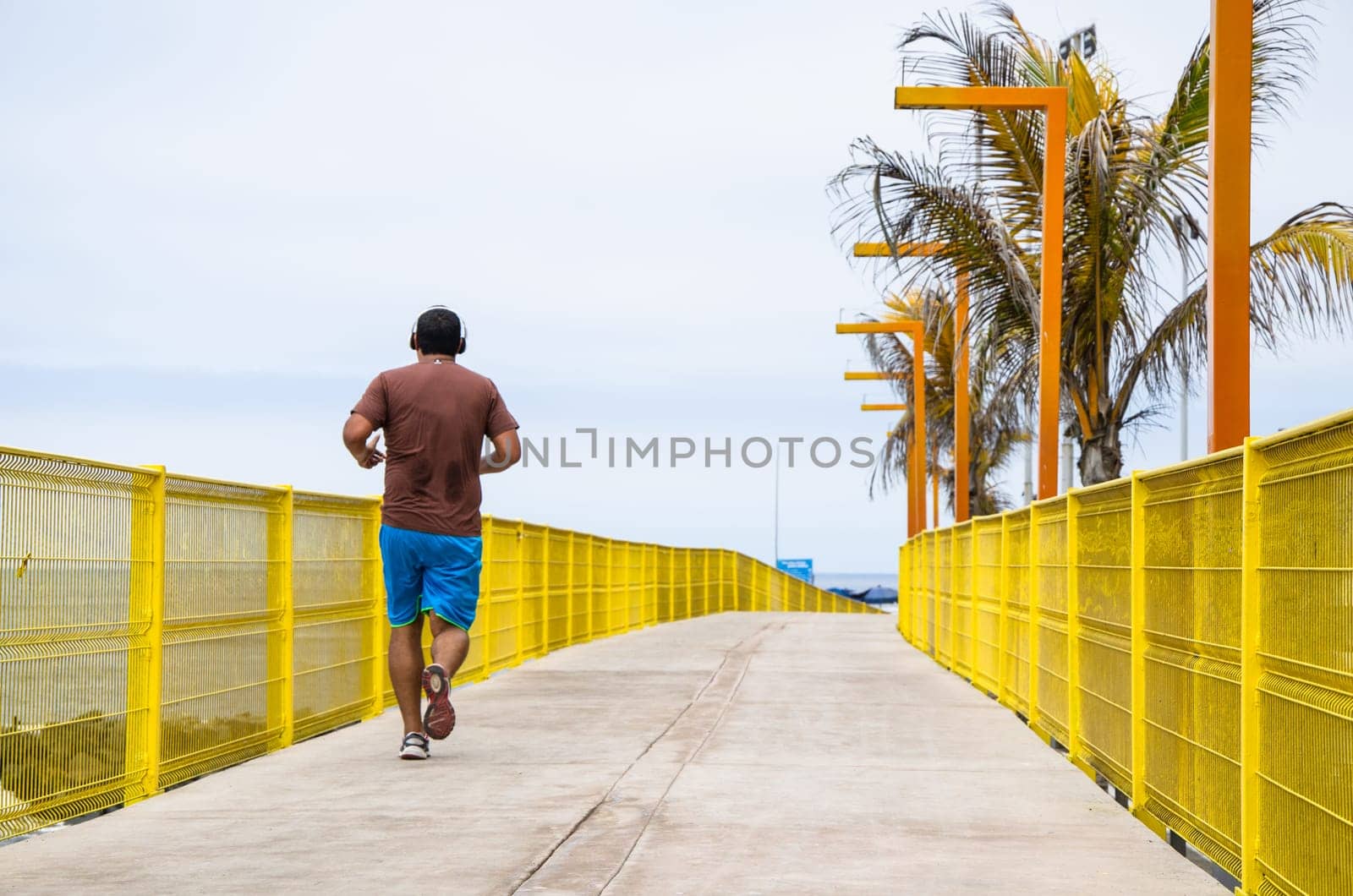 A young man listening to music and running along the beach near the ocean in the morning. by Peruphotoart