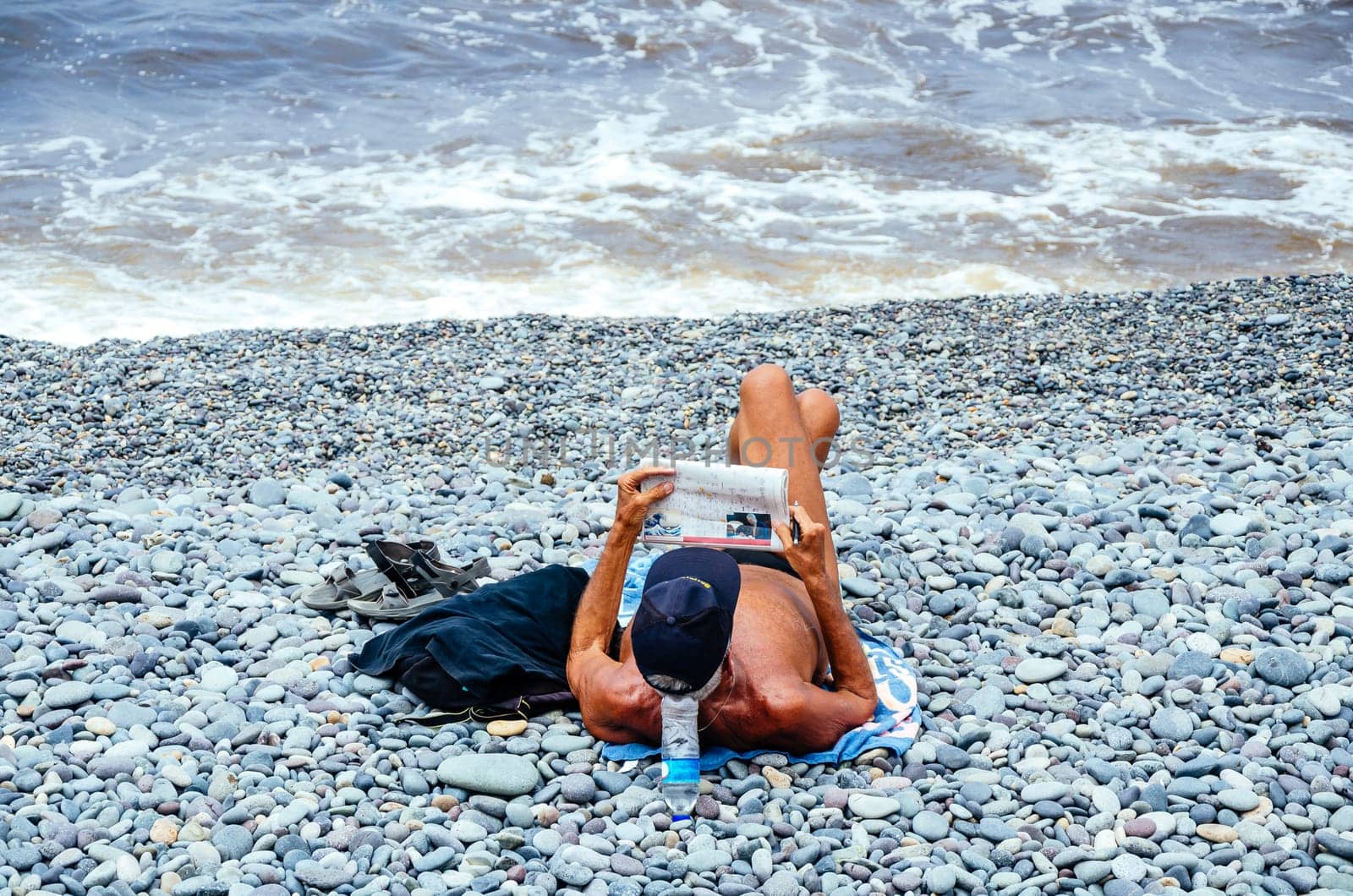 Man reading newspaper on a stones beach