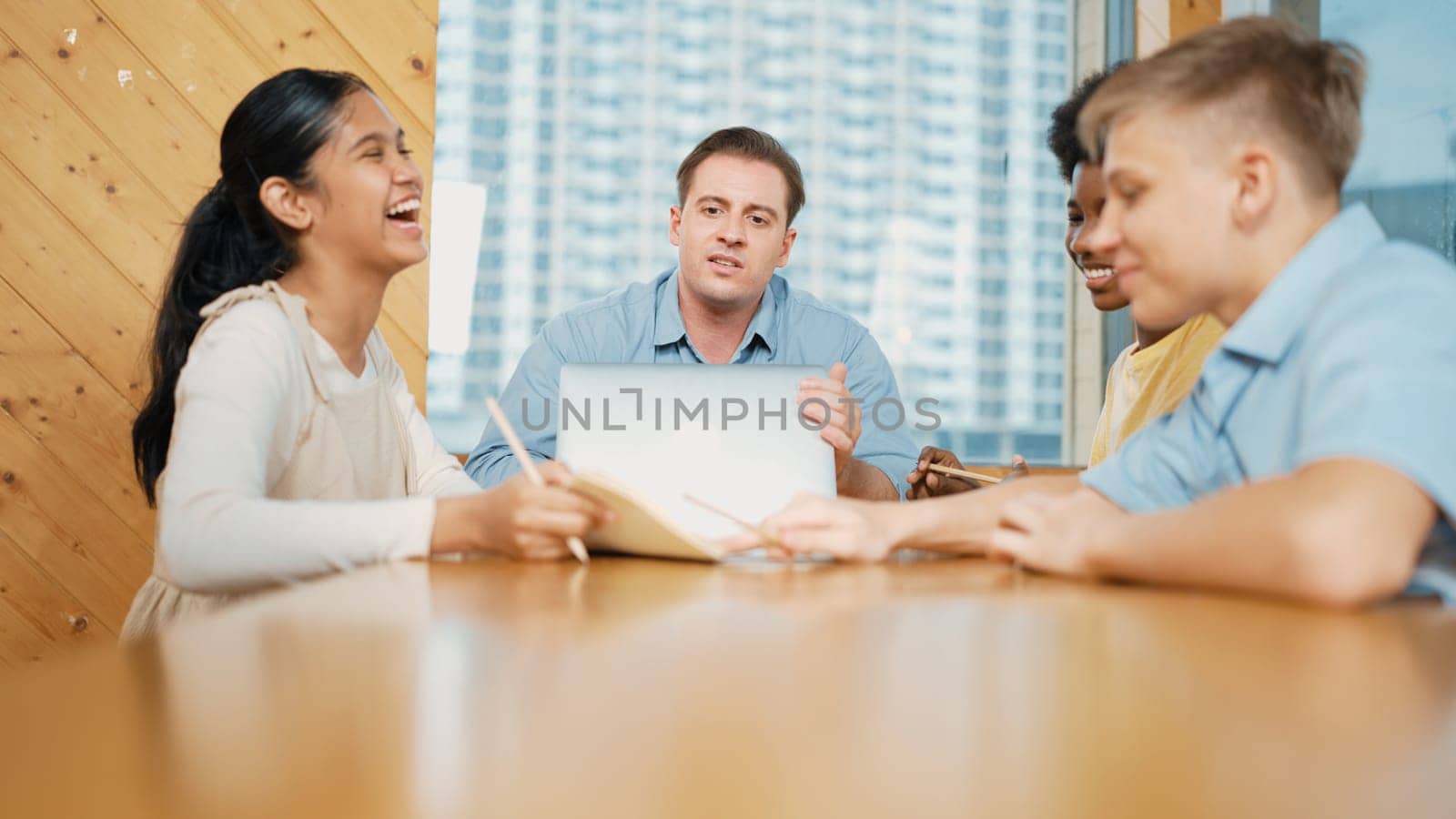 Smart teacher giving listening highschool boy present classwork at classroom while pointing at notebook. Diverse student listening classwork presentation while cute happy girl hold book. Edification.