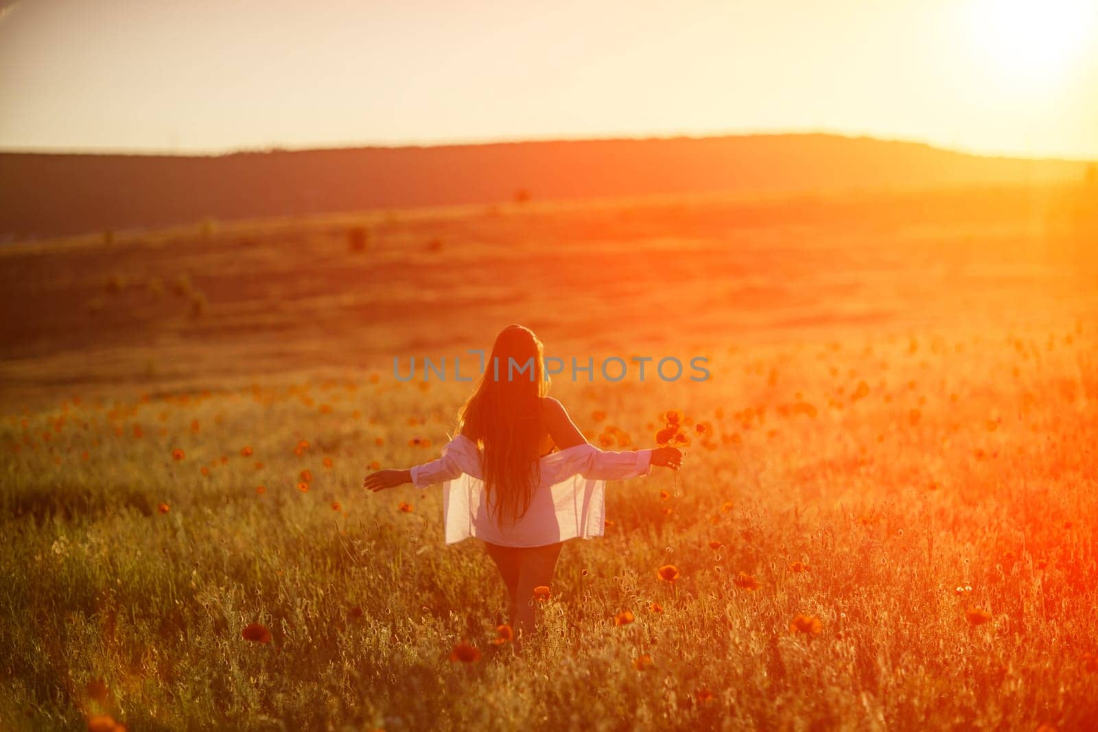 A woman is standing in a field of flowers, with the sun shining brightly on her. Concept of peace and tranquility, as the woman is enjoying the beauty of nature. by Matiunina