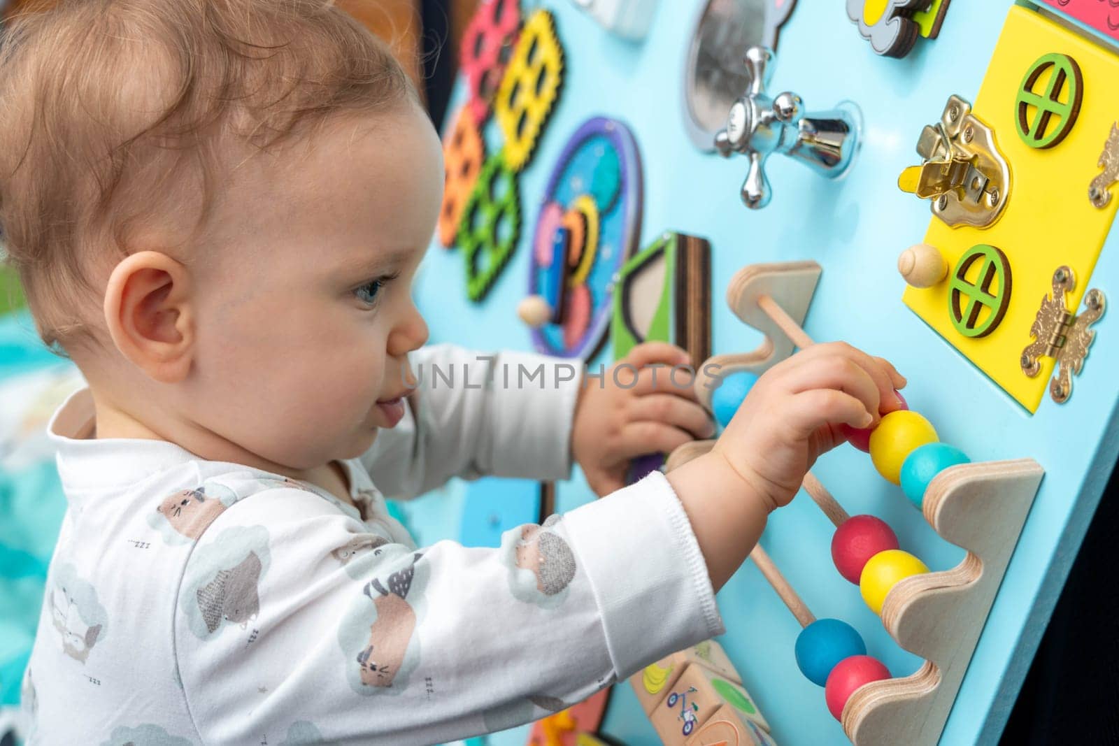 Close-up of a cute toddler playing with wooden elements on a busy board.