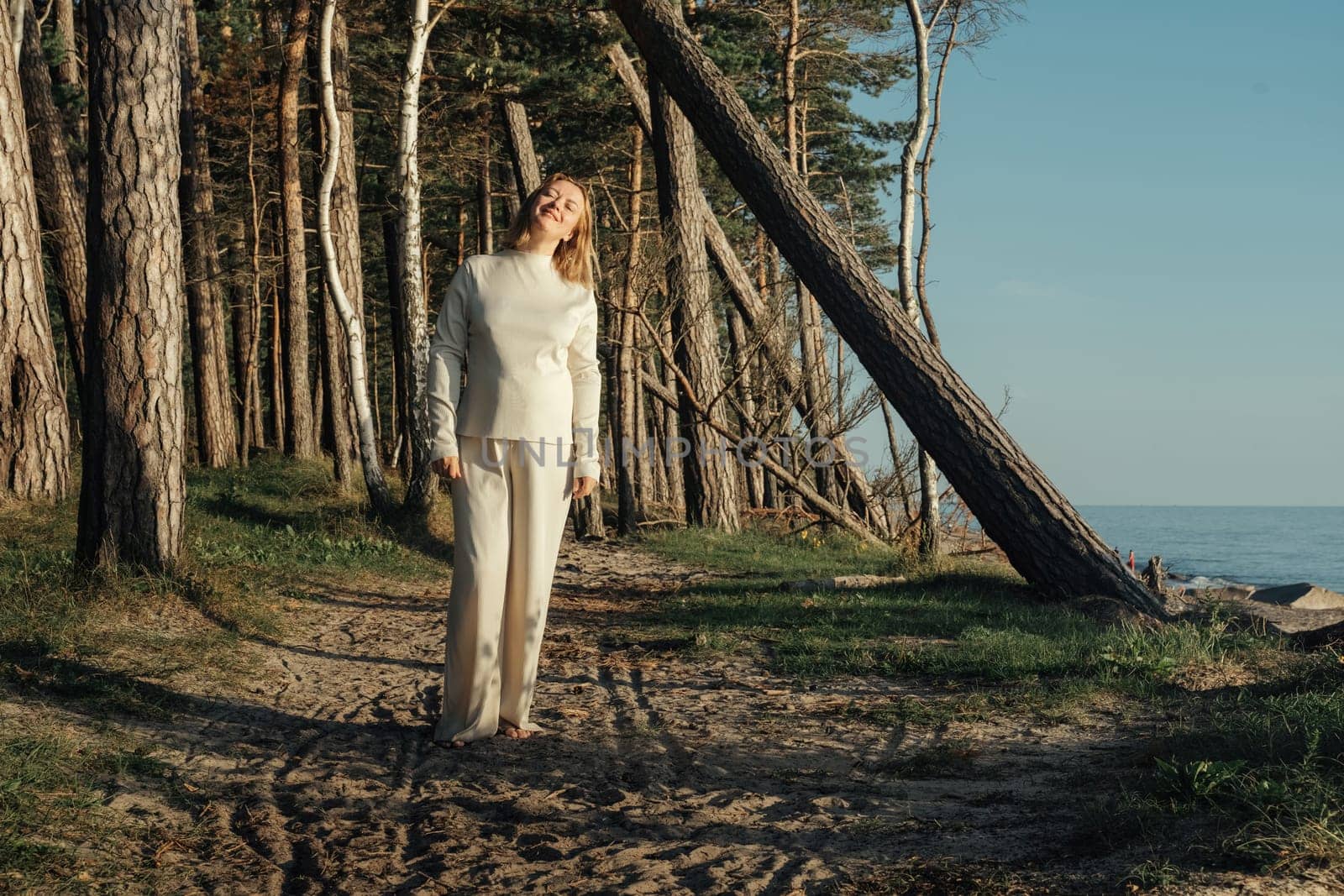 A woman dressed in white clothing is walking down a path, surrounded by nature.