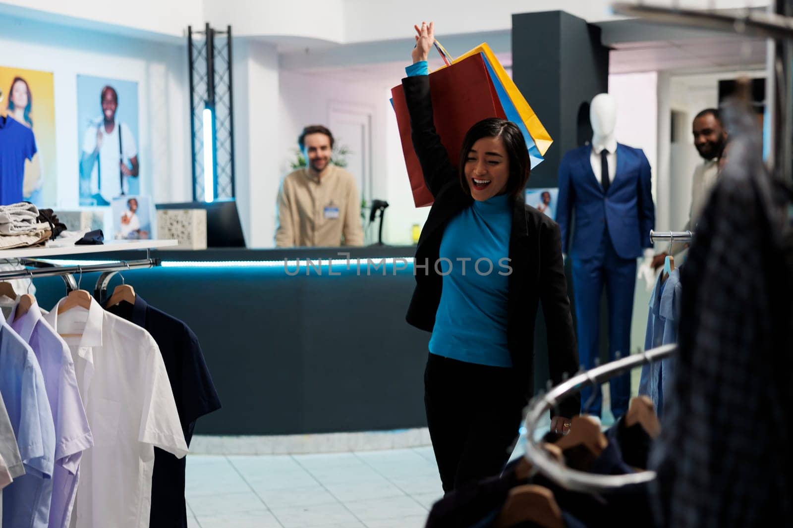 Happy woman making dance moves with shopping bags after buying garment in clothing store. Fashion boutique smiling asian customer raising hand with paper packages of purchases