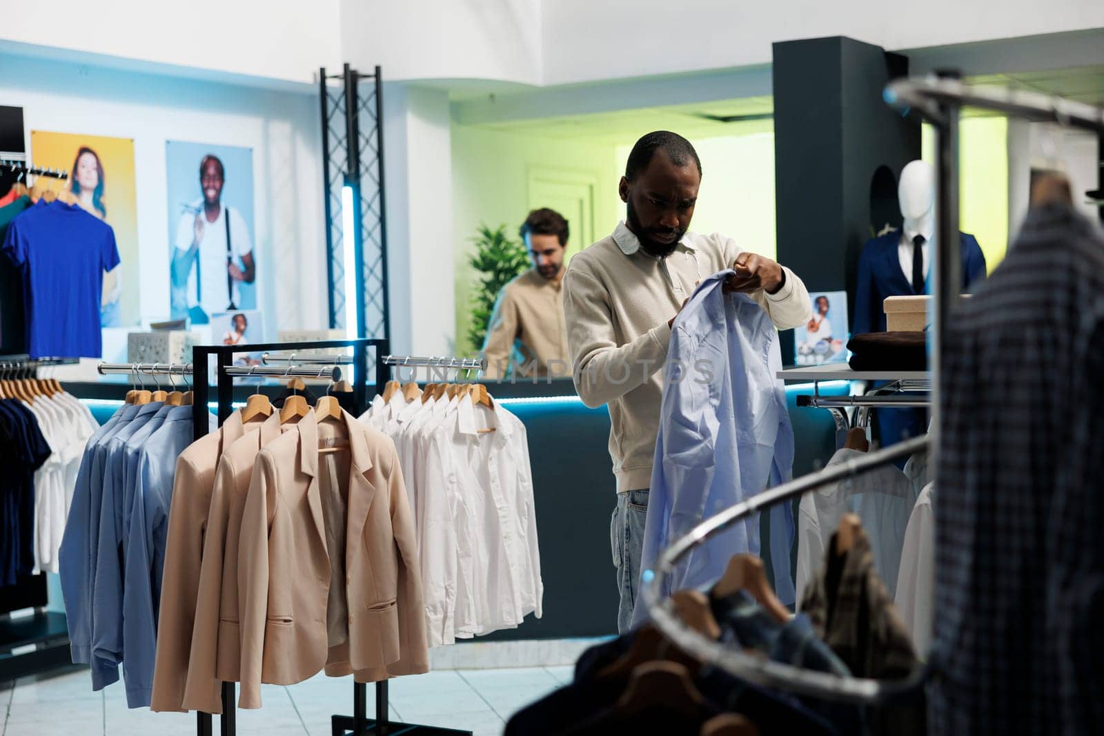 African american buyer checking size on shirt label while choosing trendy formal wear in shopping mall boutique. Young man browsing fashionable apparel on hanger in showroom