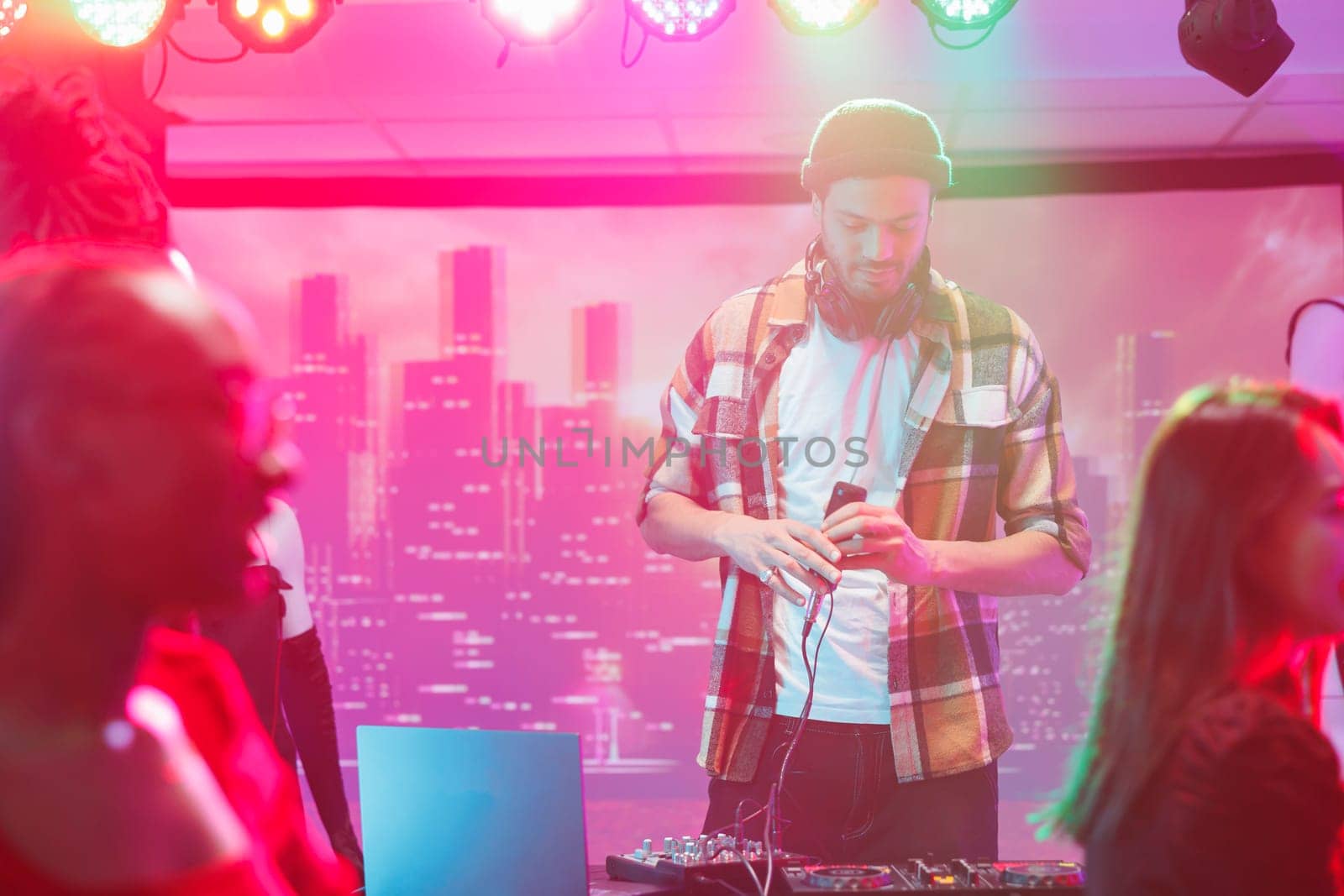 Young man musician using dj controller on stage during live concert in nightclub. Performer mixing electronic music tracks for clubbers at discotheque party in club at night