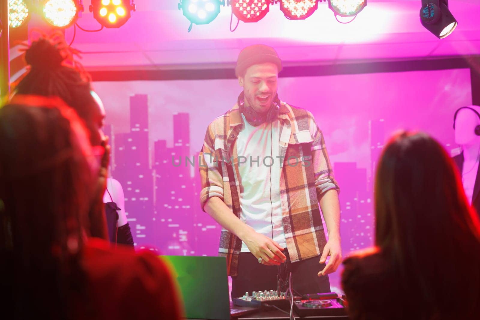 Dj on stage controlling music while crowd partying and dancing in nightclub. Man musician mixing sound on console while performing at live concert in club with spotlights
