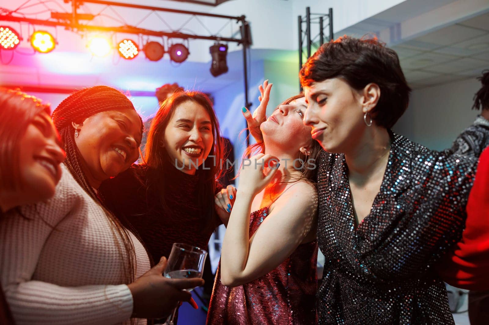 Cheerful smiling women drinking alcohol, hugging and partying together in nightclub. Carefree diverse girlfriends holding beverage glasses, laughing and having fun in club